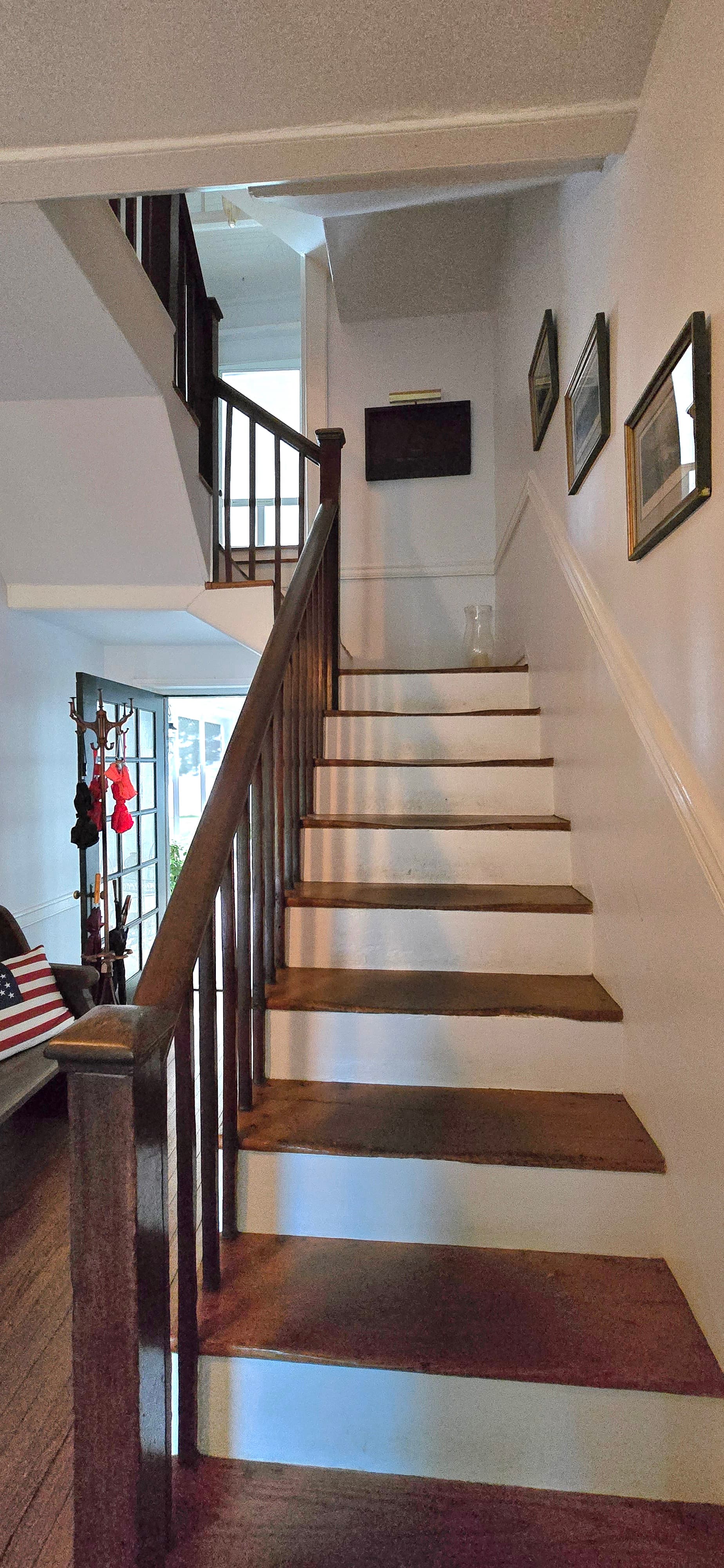 A staircase with wooden steps leads to an upper level in a well-lit hallway adorned with framed pictures.