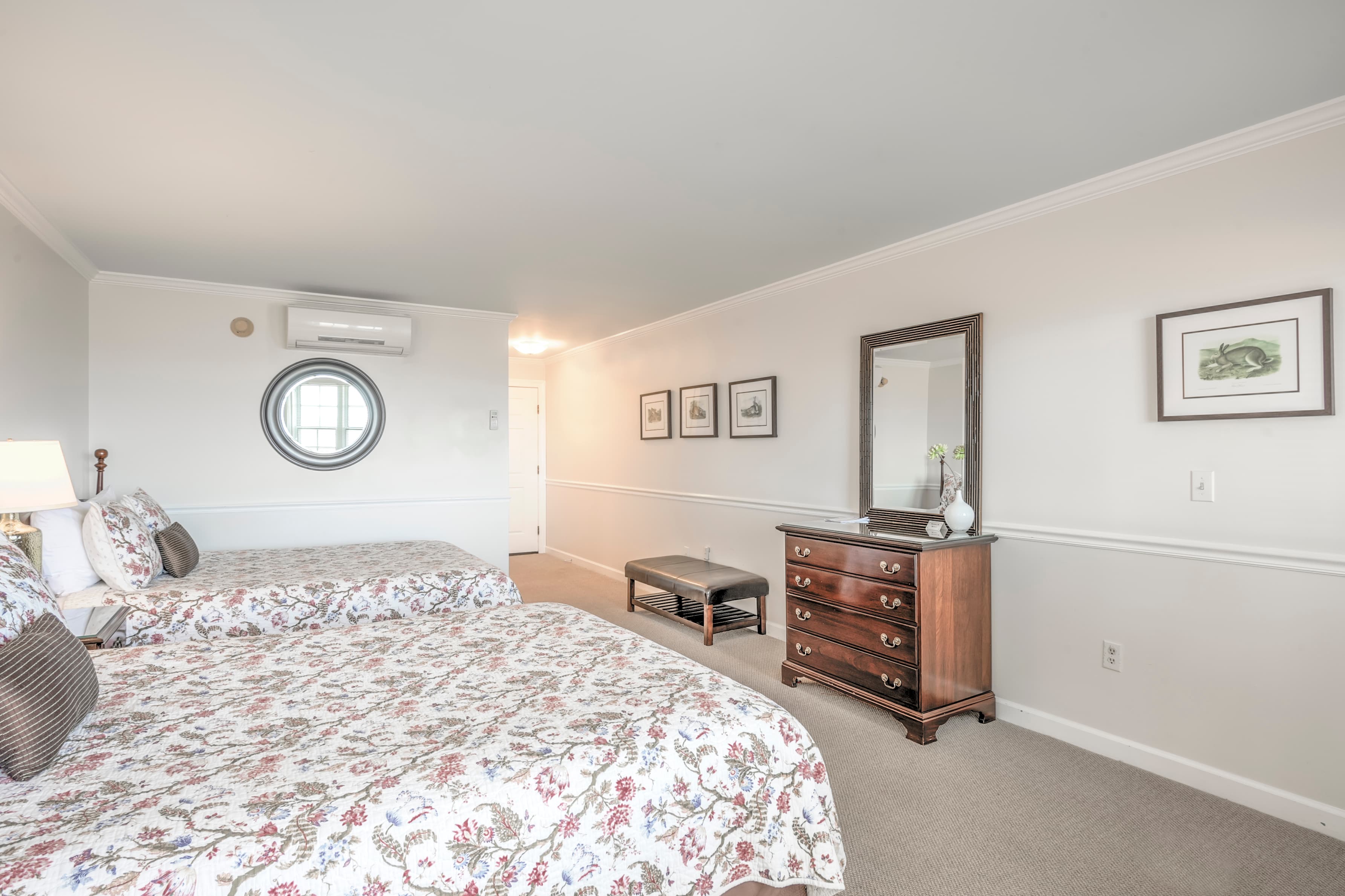 A spacious bedroom featuring two floral-patterned beds, a dresser, and a round window.