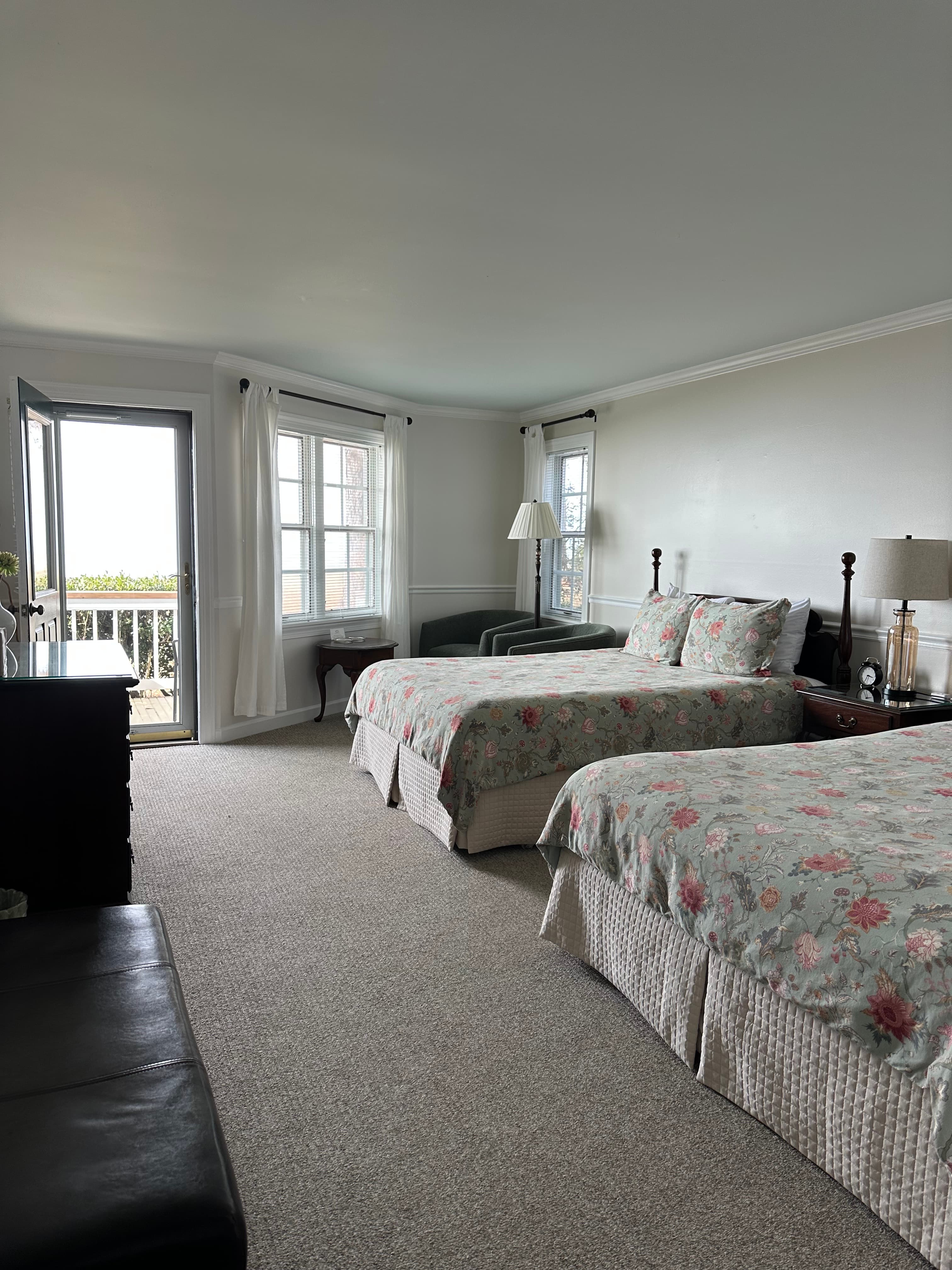 A well-lit bedroom featuring two floral-patterned twin beds and a balcony door.