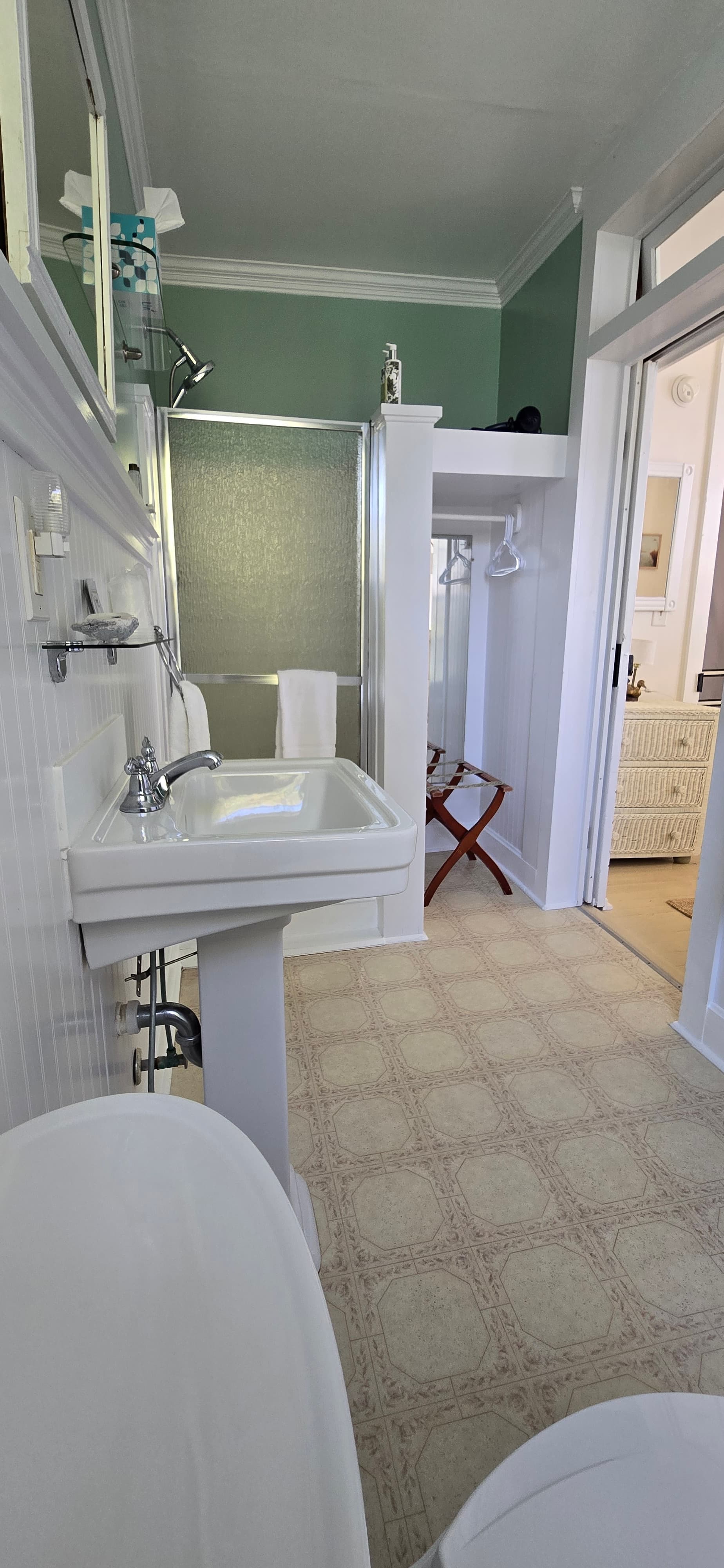 A spacious bathroom featuring a sink, shower, and a decorative stool with light-colored flooring.