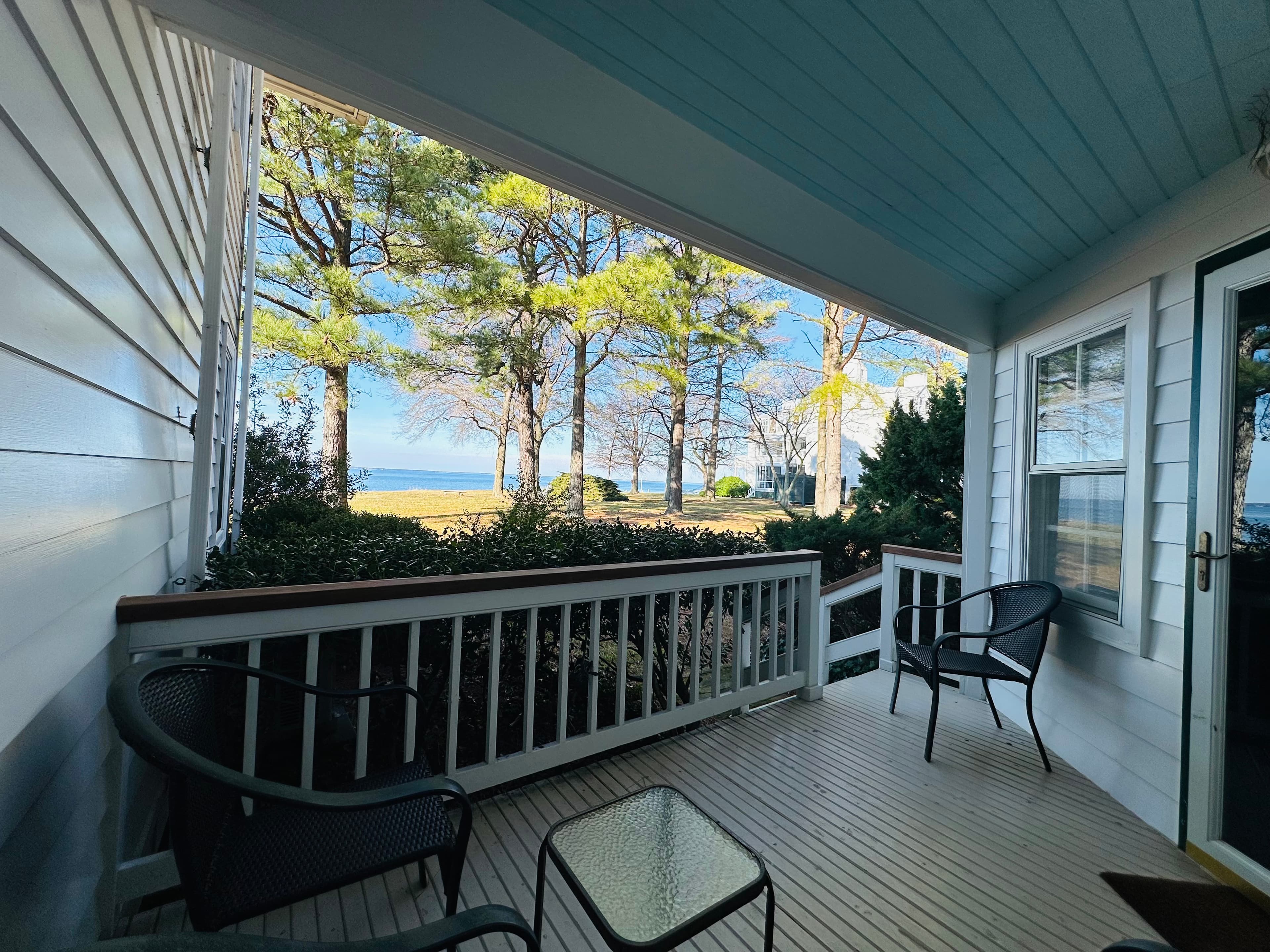 A cozy porch overlooking a beach with trees and a clear blue sky.