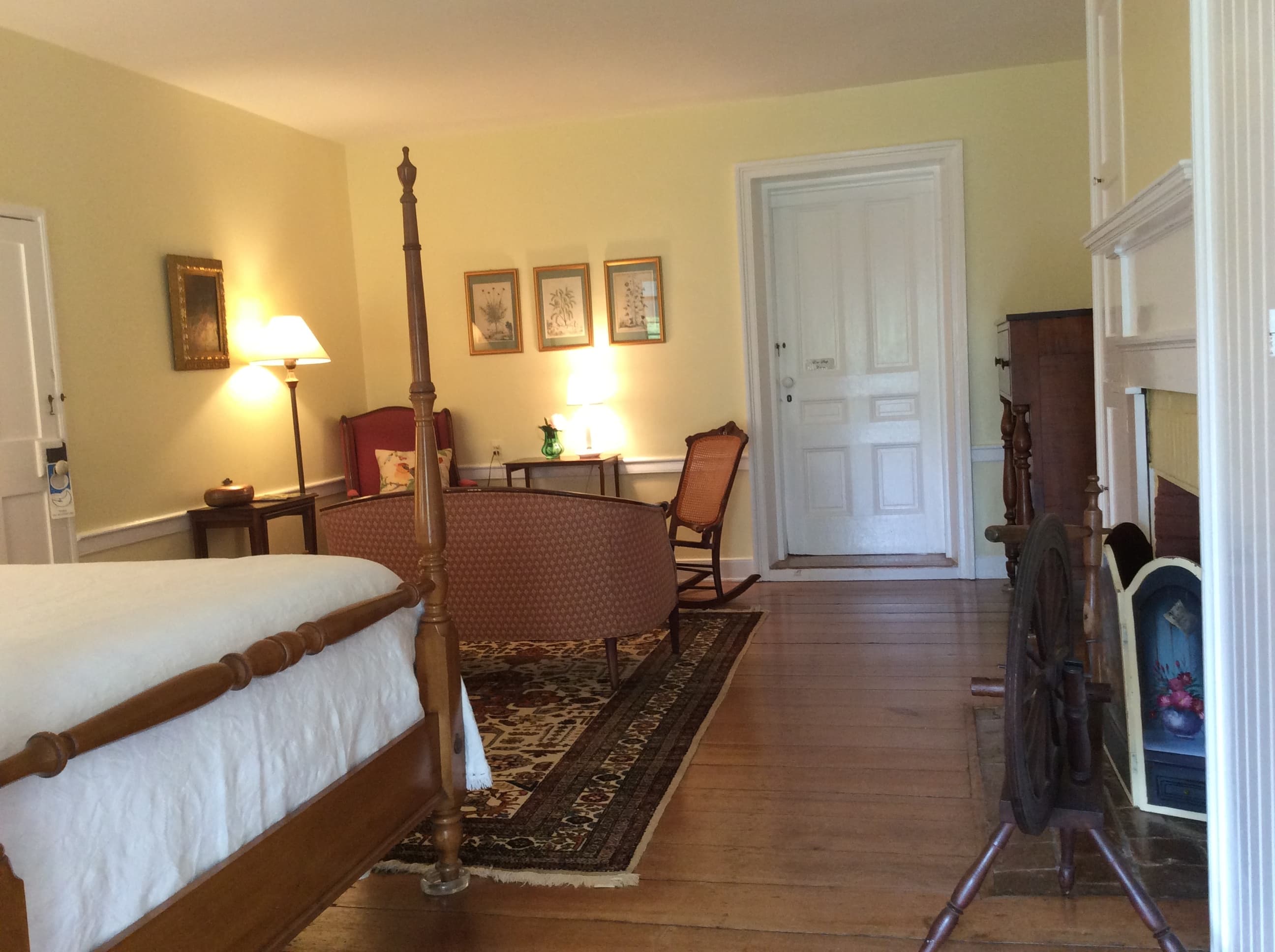 A cozy room featuring a wooden bed, seating area, lamp, and decorative art on soft yellow walls.