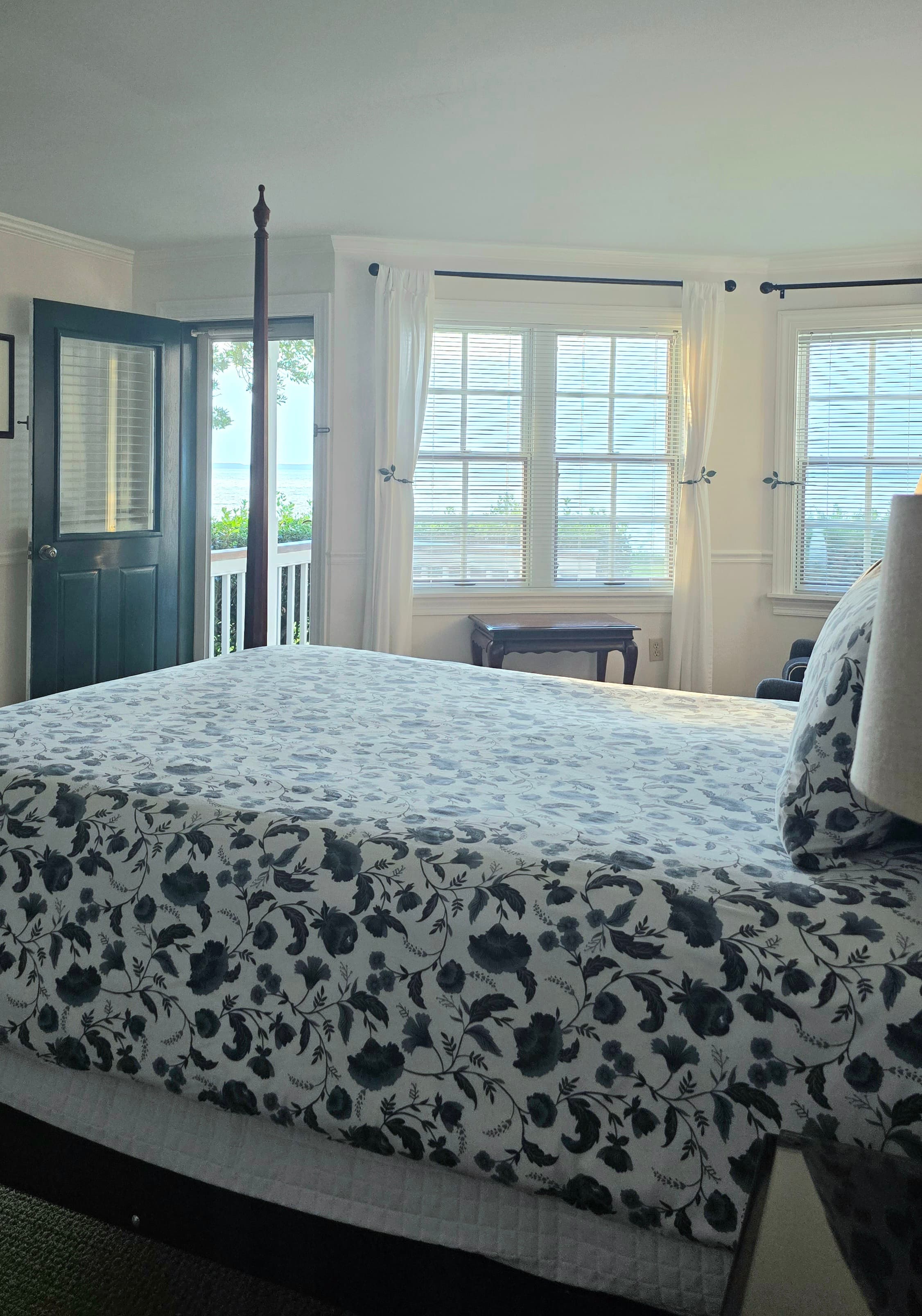 A cozy bedroom featuring a floral-patterned bedspread and large windows with sheer curtains.