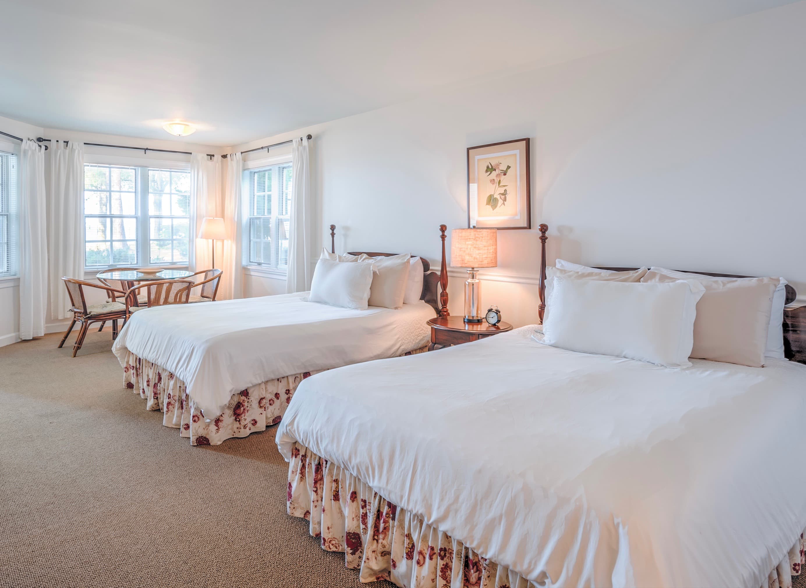 A cozy hotel room featuring two beds, a small dining area, and large windows for natural light.
