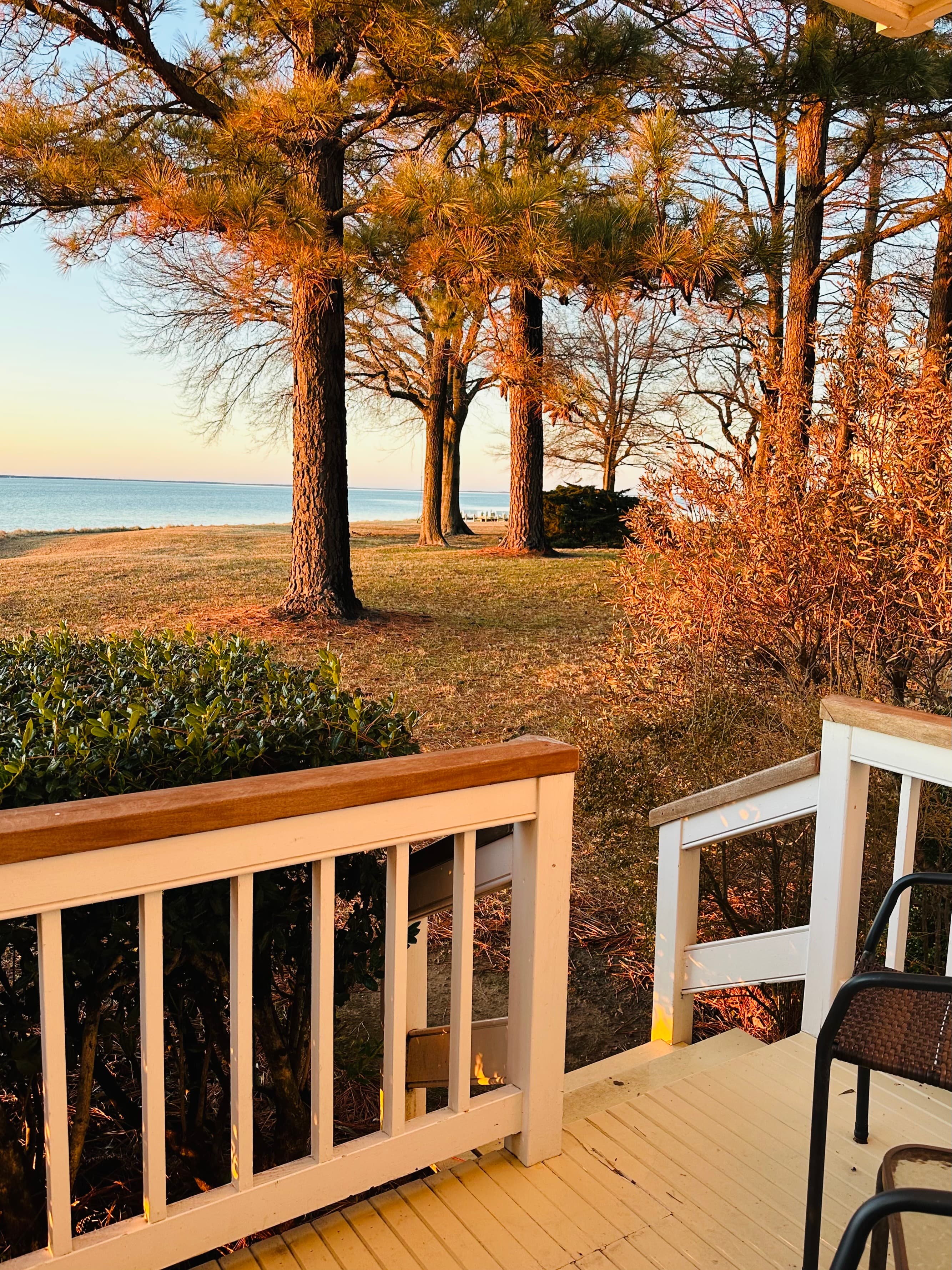 A view from a porch overlooking a tranquil lake framed by trees during sunset.