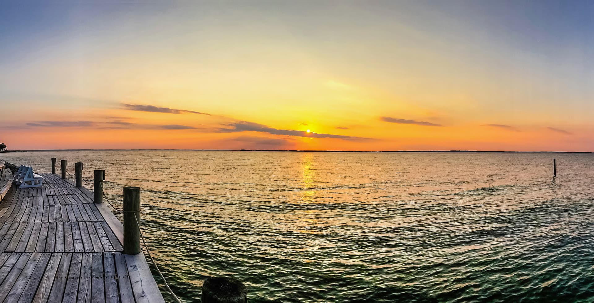 A serene sunset over calm waters viewed from a wooden dock.