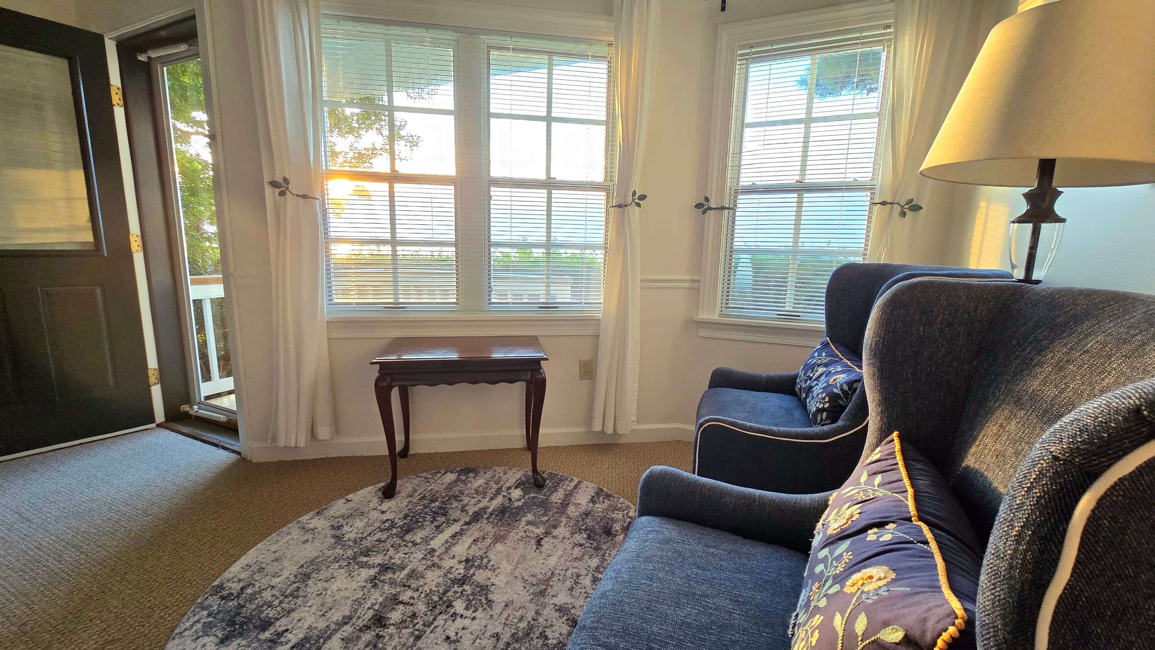 Cozy living room with a blue sofa, a small table, and large windows letting in warm sunset light.