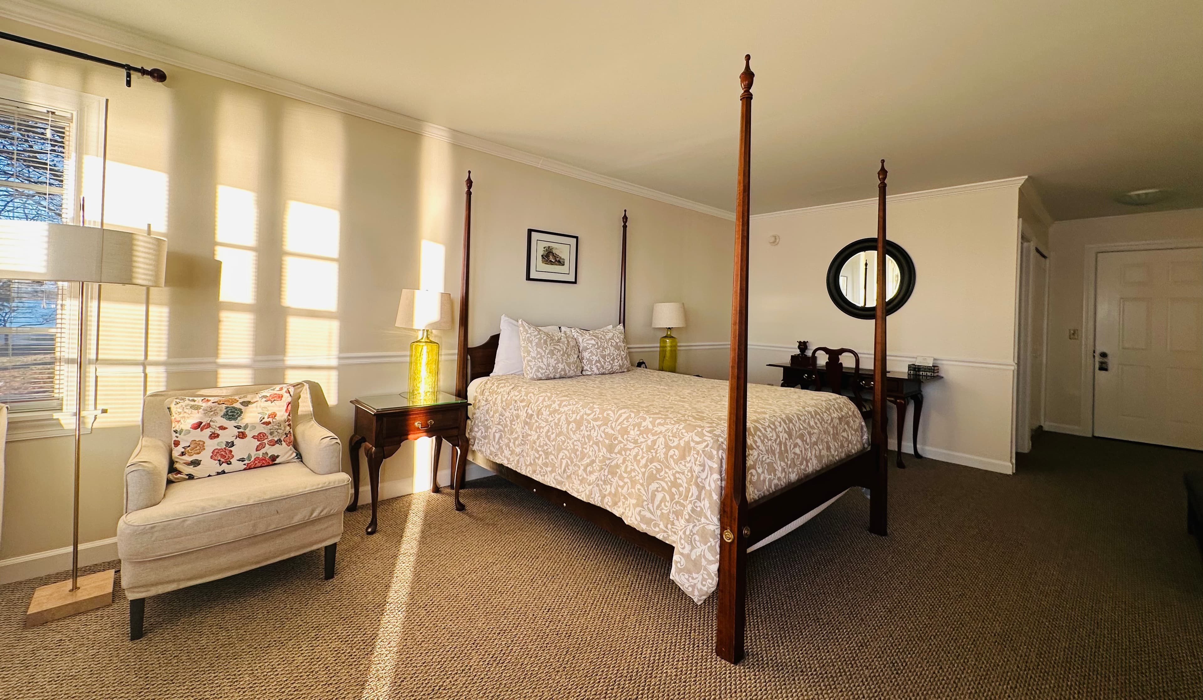 A well-lit bedroom featuring a four-poster bed, a cozy armchair, and decorative accents.