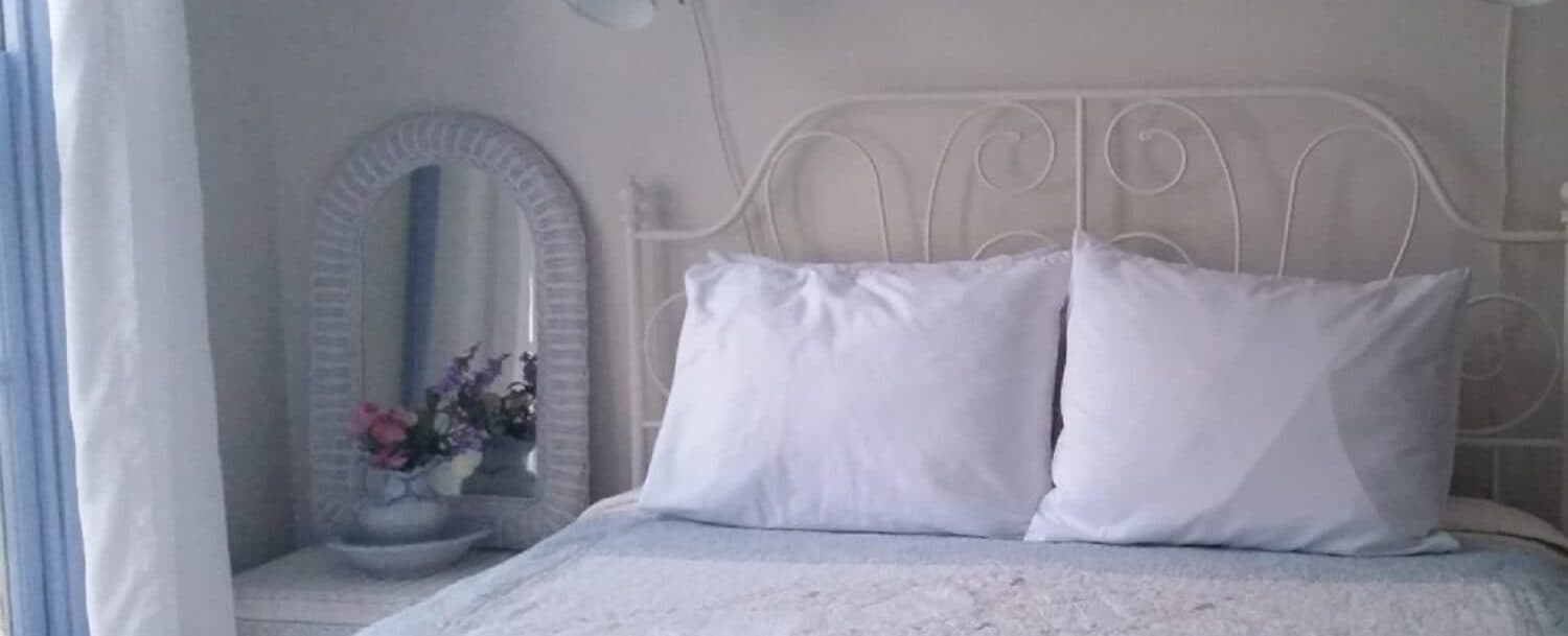 A neatly made bed with white pillows and a decorative mirror beside it.
