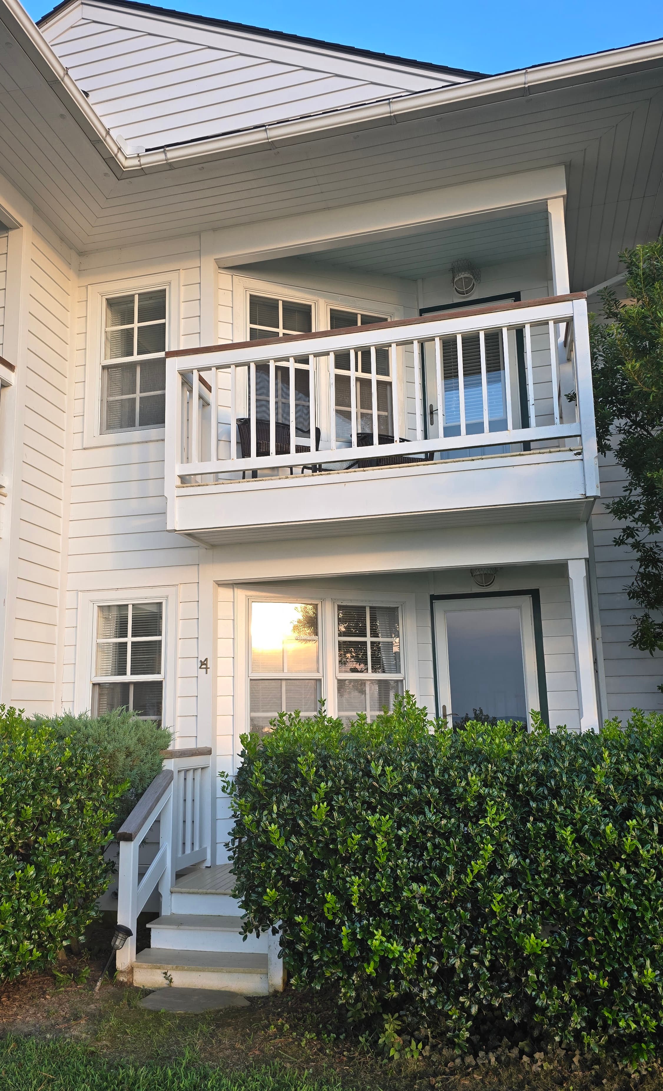 A two-story white house with a balcony overlooking a lush green shrub.