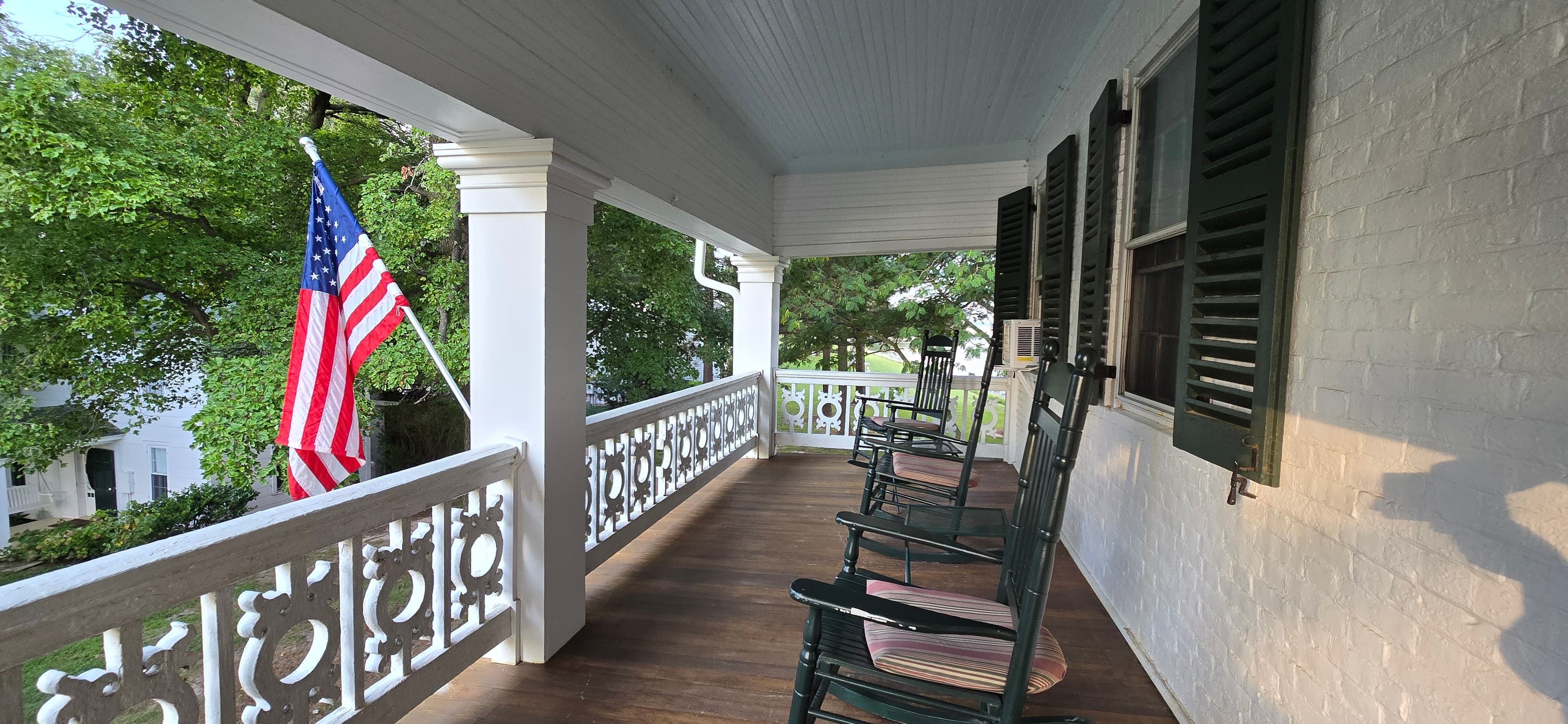 A porch with rocking chairs lined up and an American flag waving in the breeze.