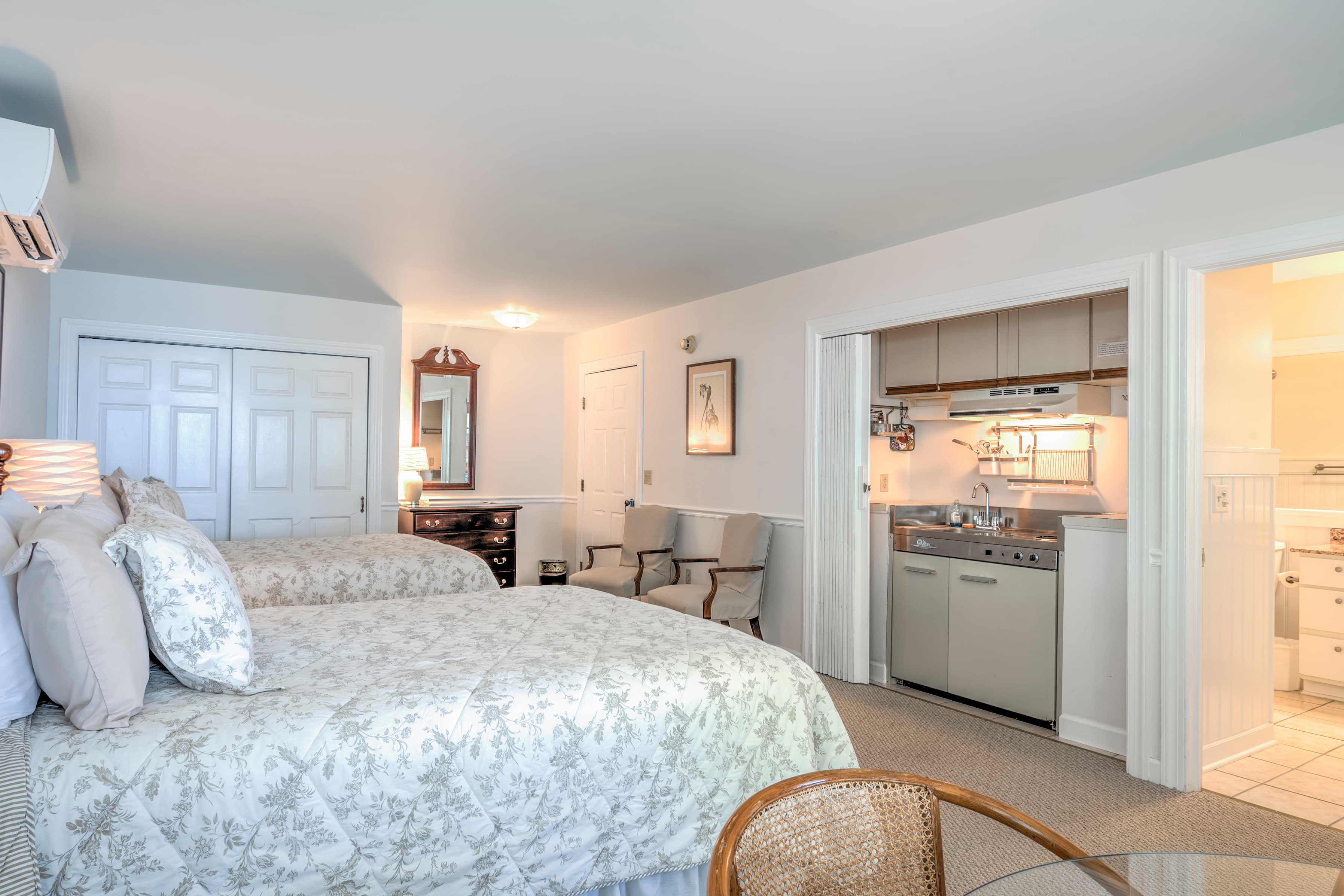 A spacious hotel room featuring two beds, a kitchenette, and an attached bathroom.