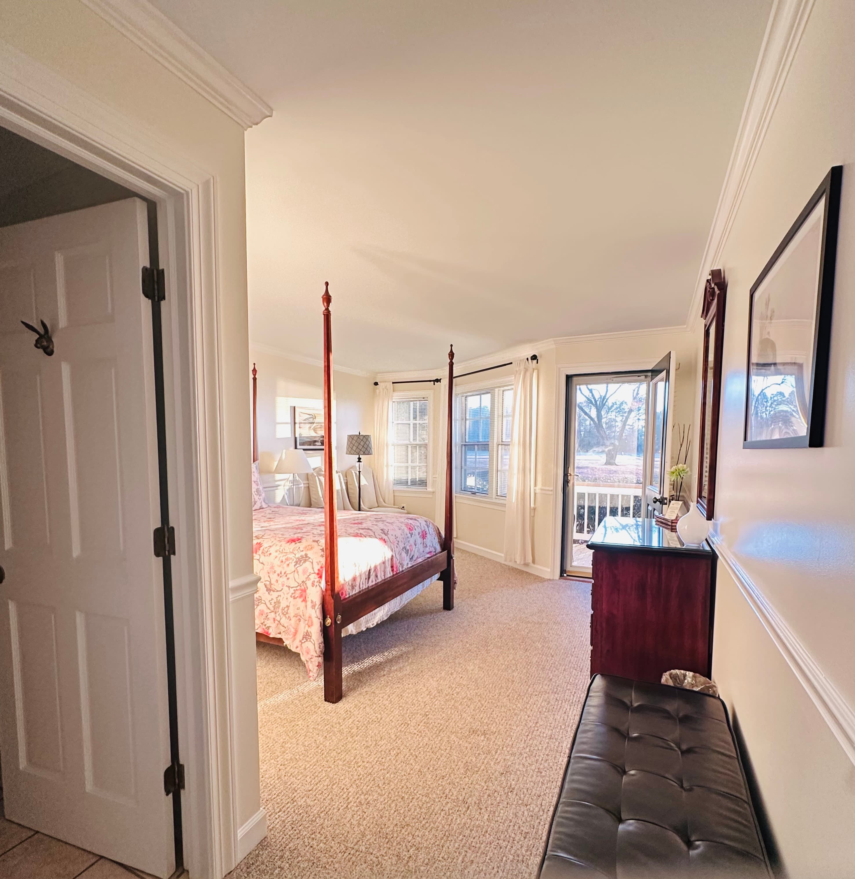 A bright, open bedroom with a four-poster bed, large windows, and a view of the outdoors.