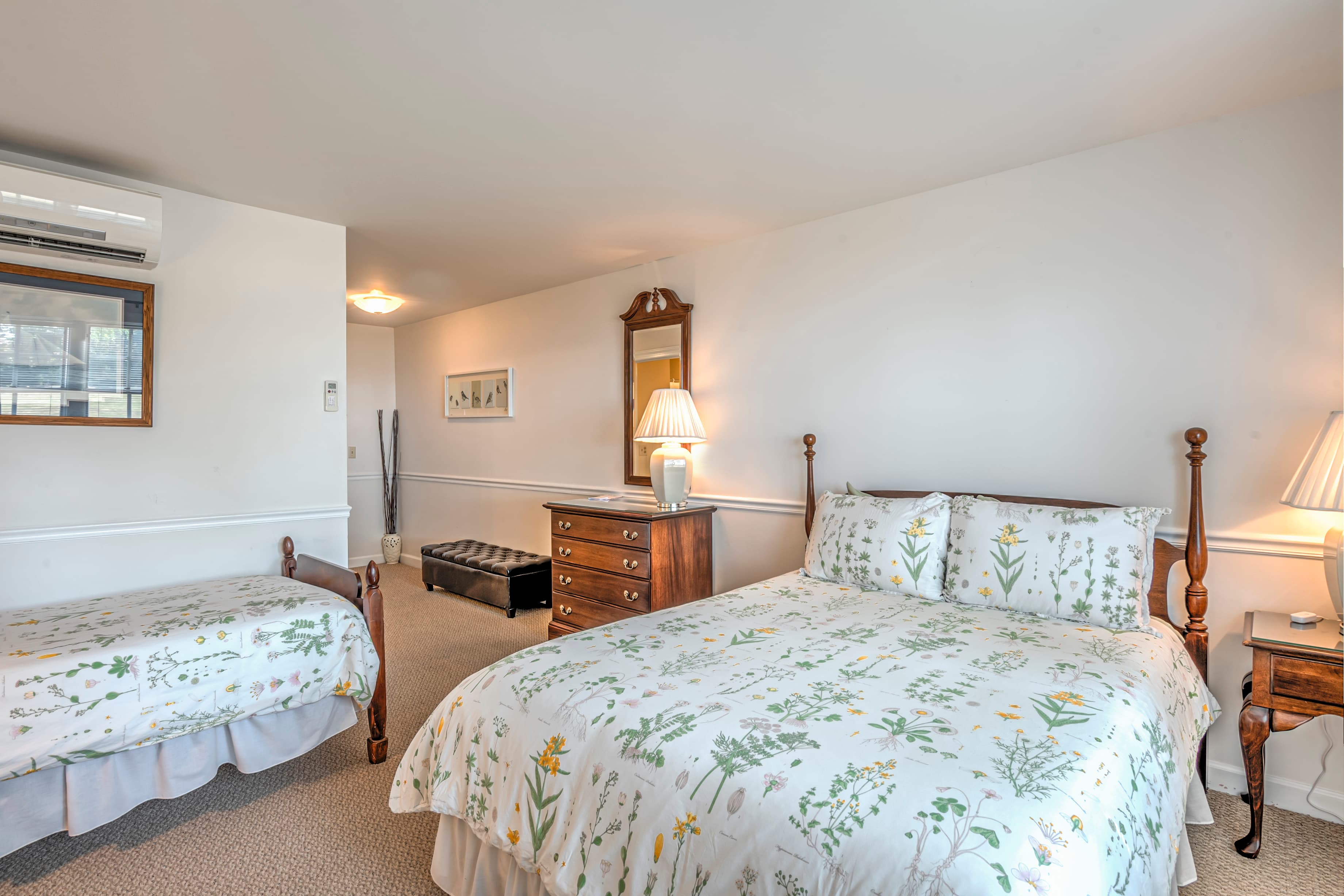 A cozy bedroom featuring a double bed and a twin bed, both with floral-patterned bedding, accompanied by wooden furniture and bedside lamps.