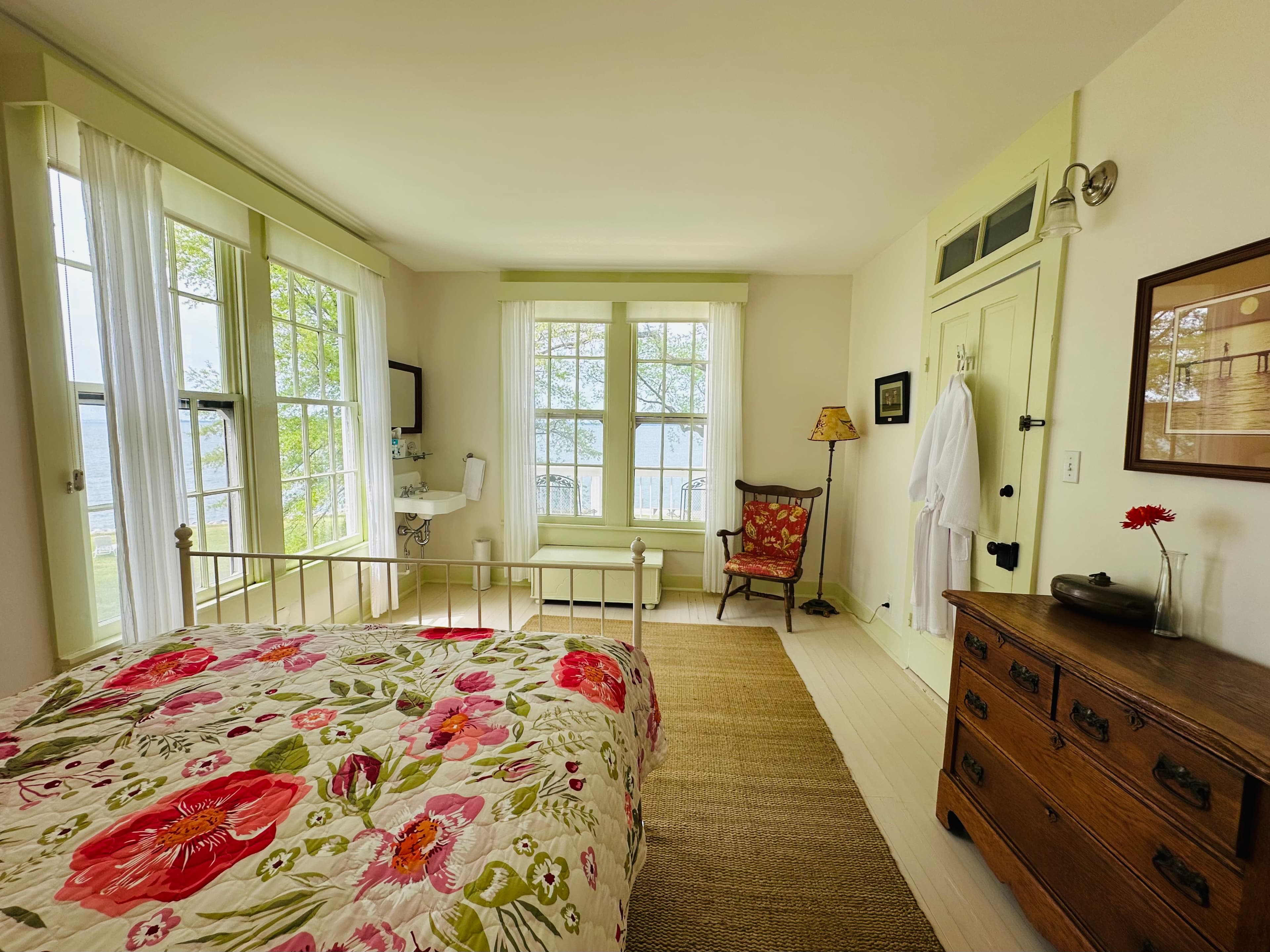 Bright and airy bedroom with floral bedding, large windows, and a vintage armchair.