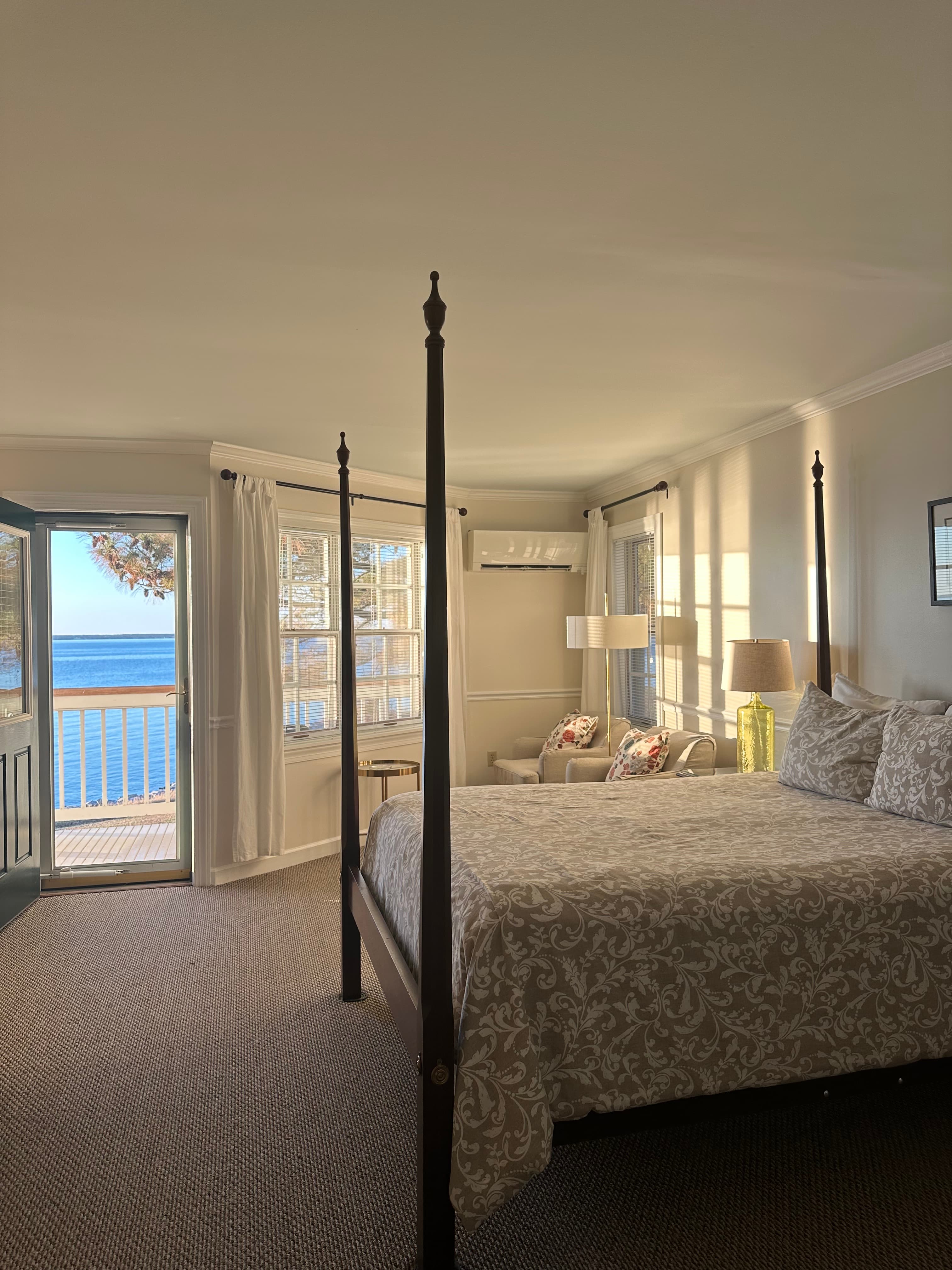 Cozy bedroom with a four-poster bed and views of a lake through open doors.