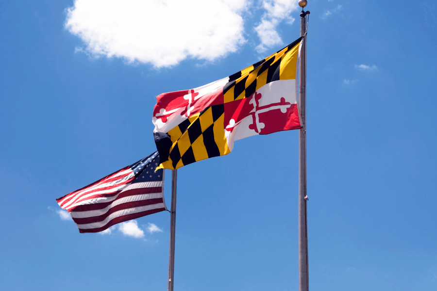 Two flags, the American flag and the Maryland state flag, flutter against a blue sky.