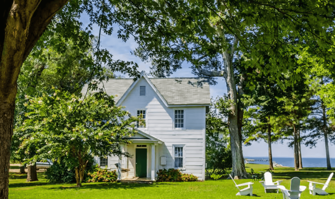 A white house surrounded by greenery with a view of the water in the background.