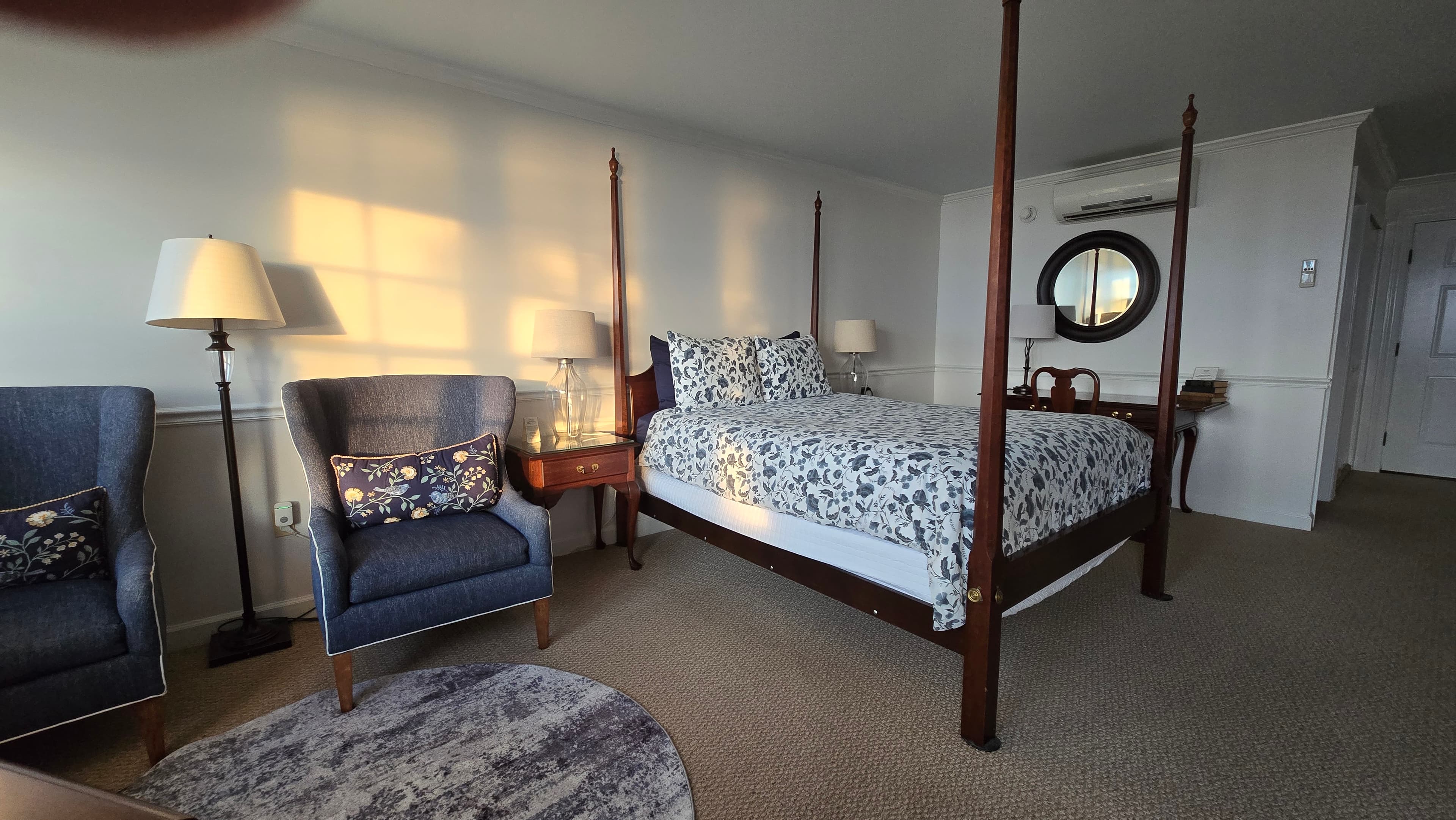 Cozy bedroom featuring a four-poster bed, two blue armchairs, and warm lighting.