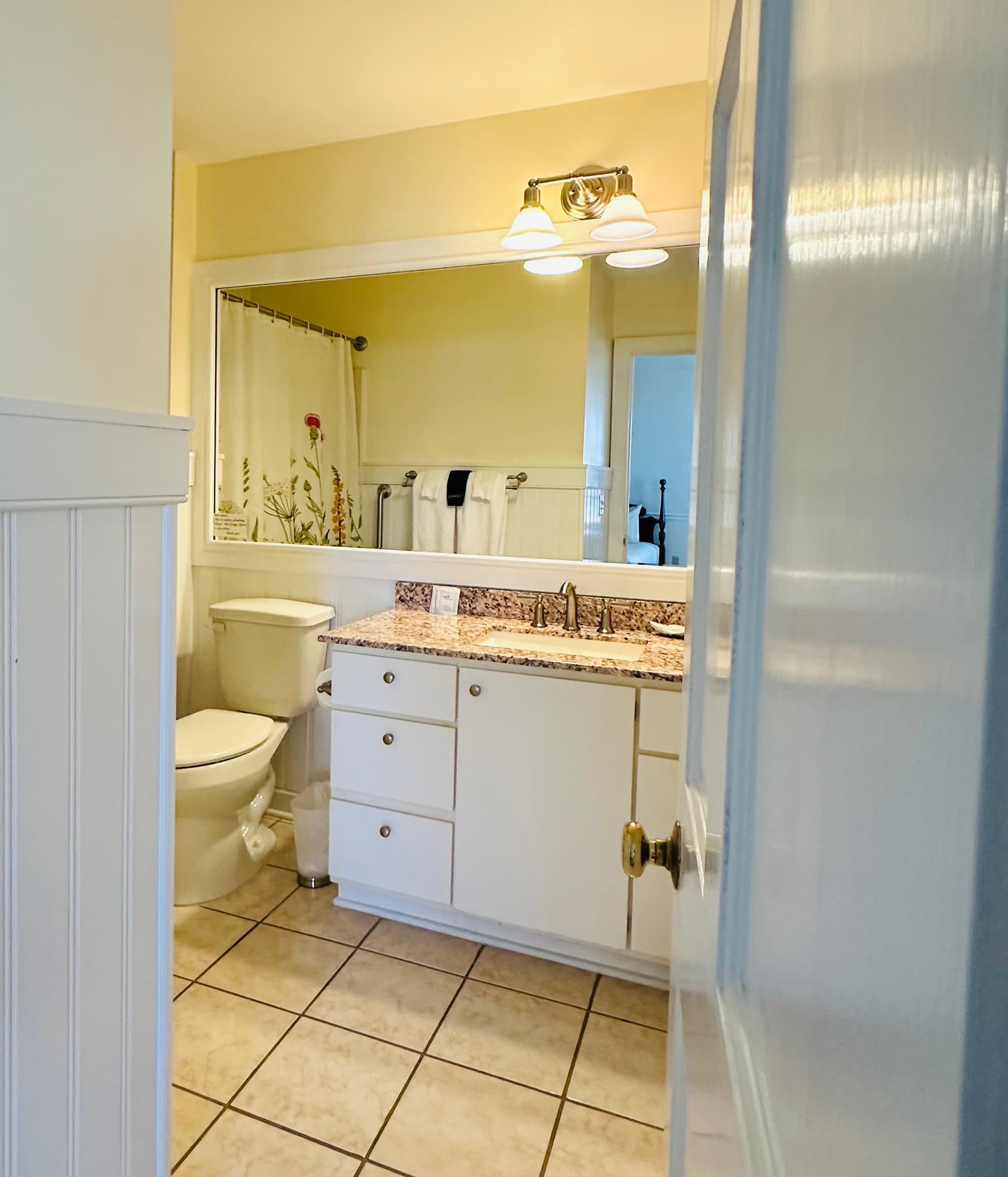 A bright, clean bathroom featuring a toilet, sink with a granite countertop, and a shower curtain with floral design.