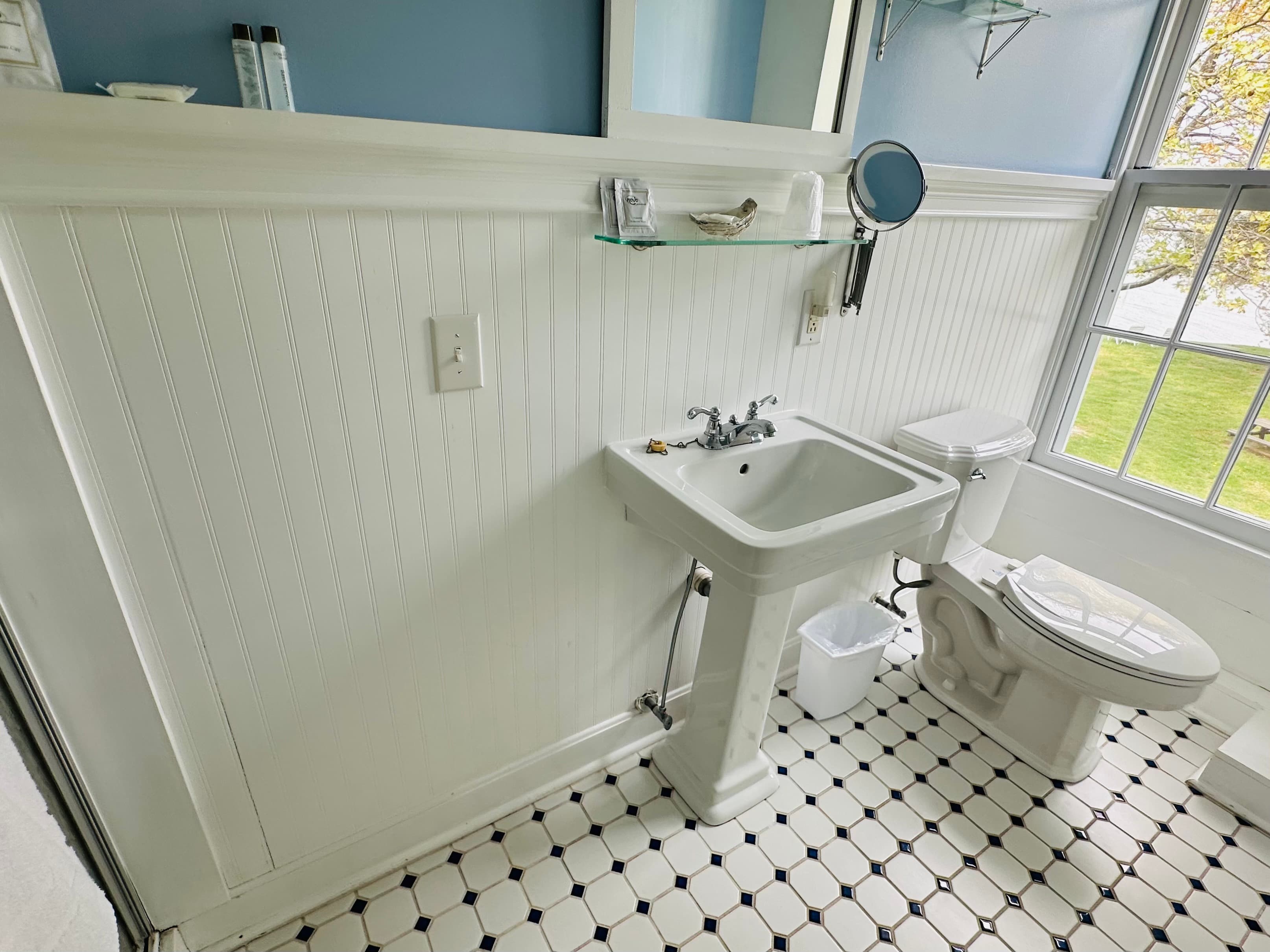 A bright bathroom featuring a pedestal sink, toilet, and window with a view.