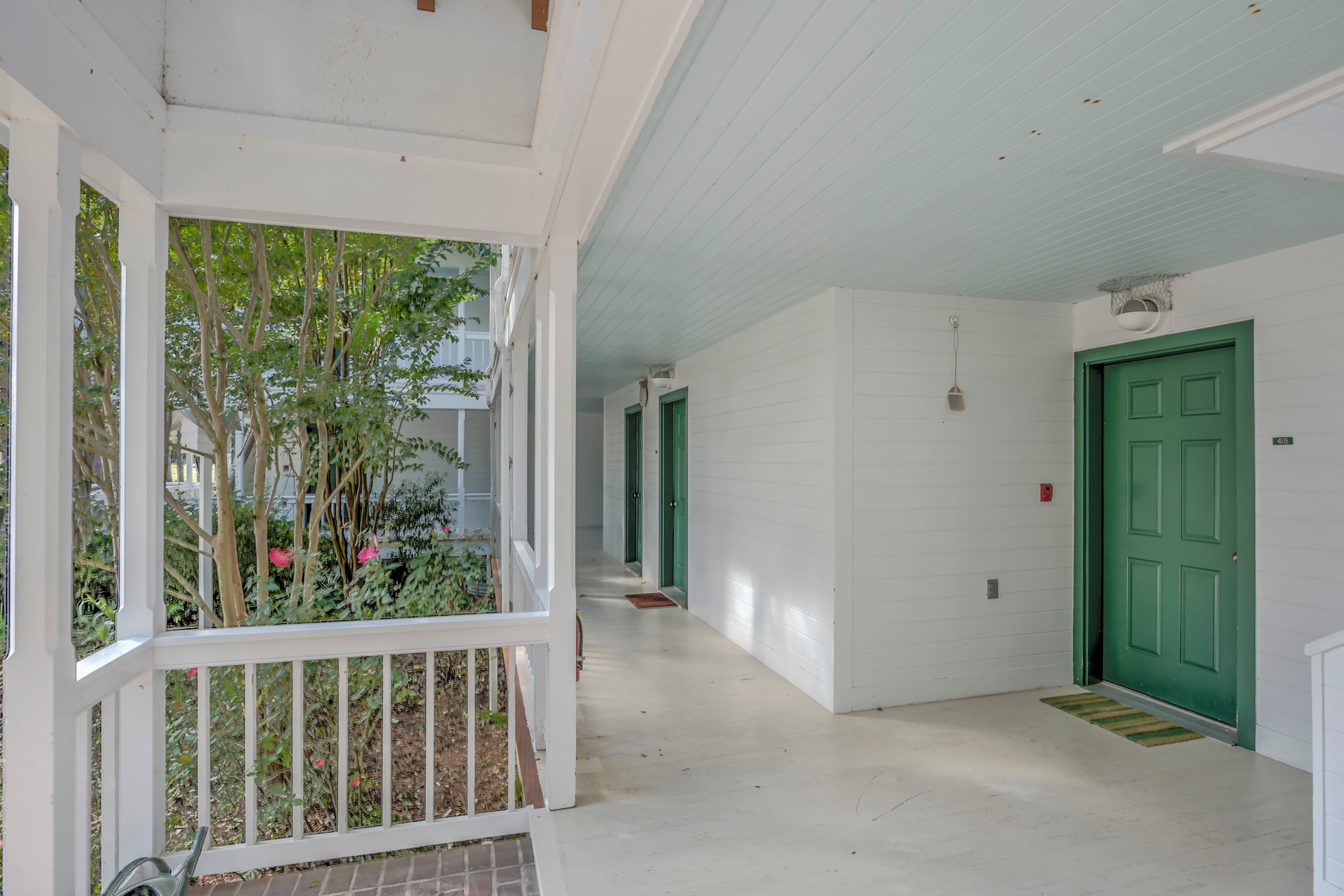 A covered porch area with green doors and a view of surrounding foliage.