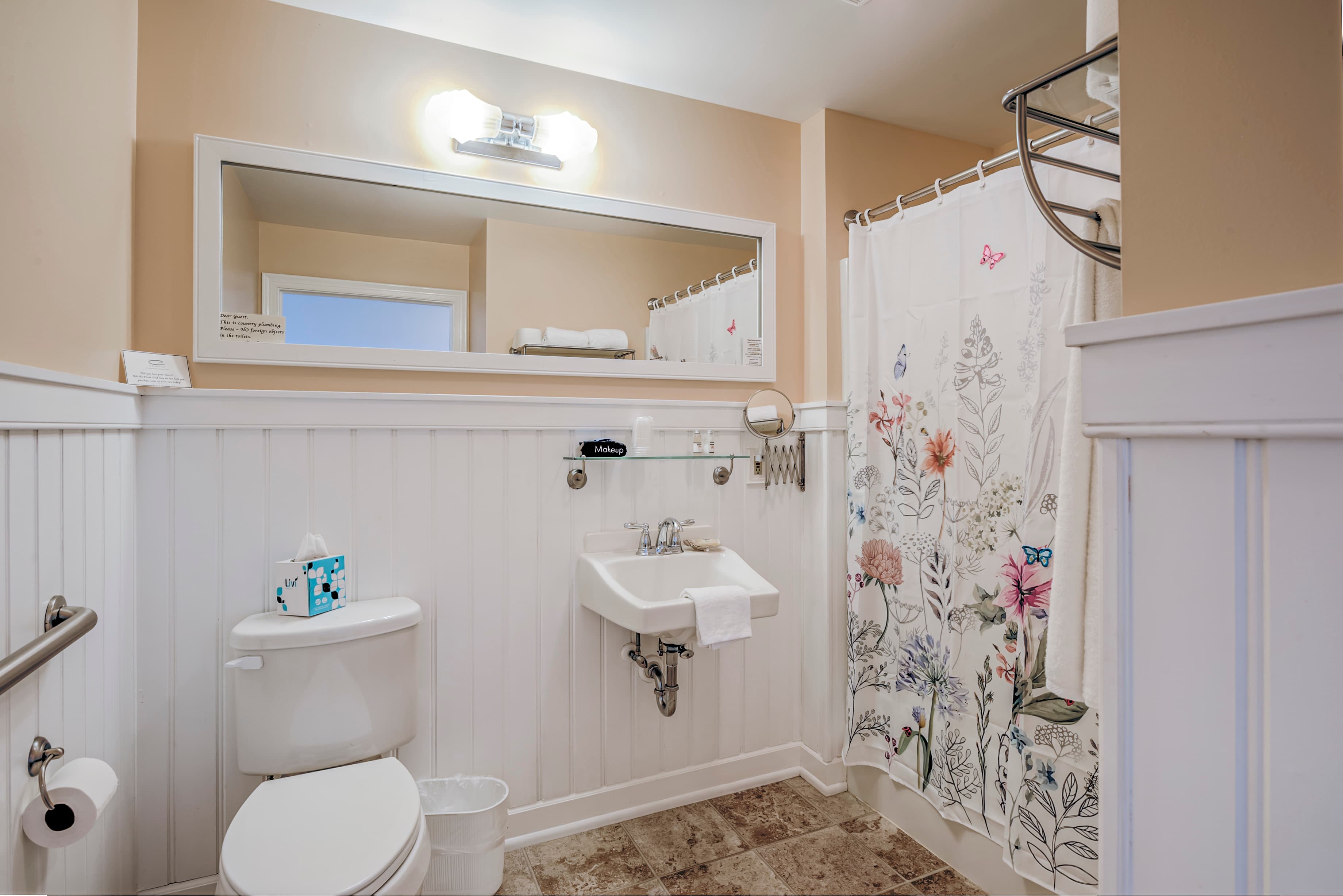 A clean bathroom featuring a shower with a floral curtain, a small sink, and a toilet against white paneling.
