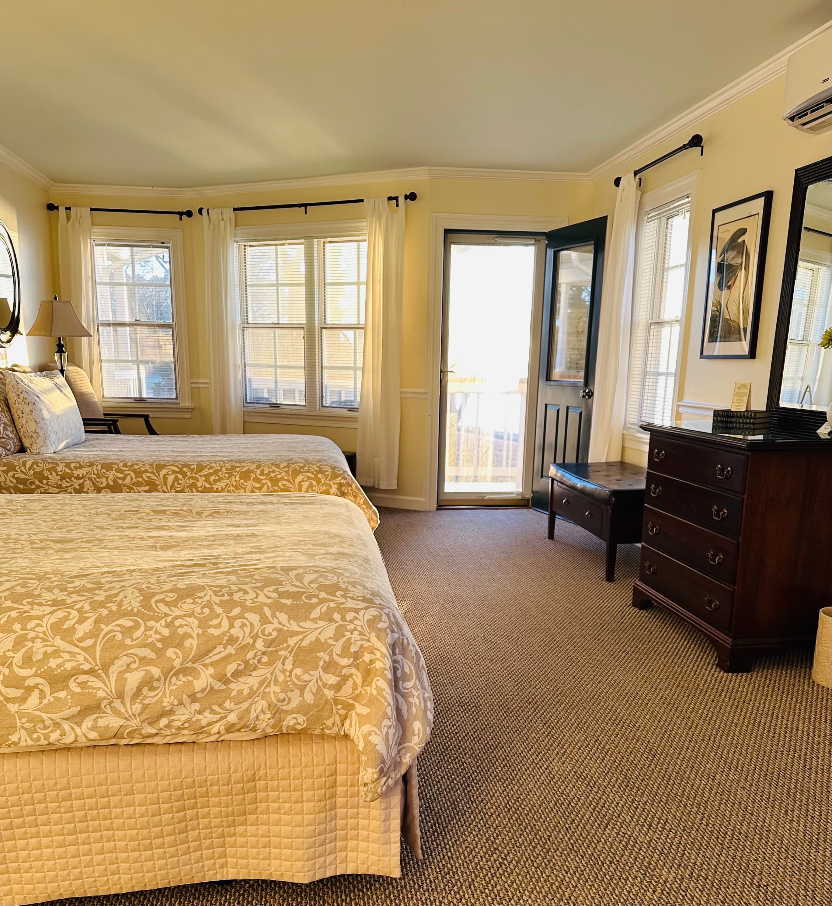 A bright and inviting hotel room featuring two beds, large windows, and a door leading to a balcony.