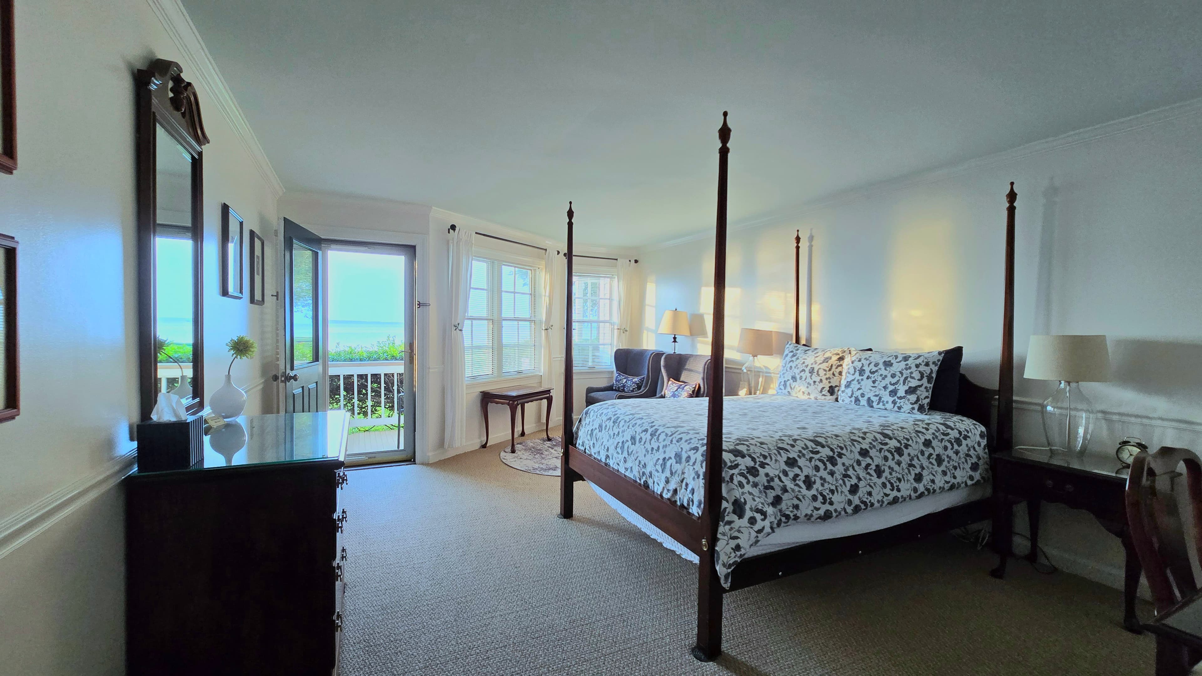 Bright and airy bedroom featuring a four-poster bed, a sitting area, and large windows with a view.