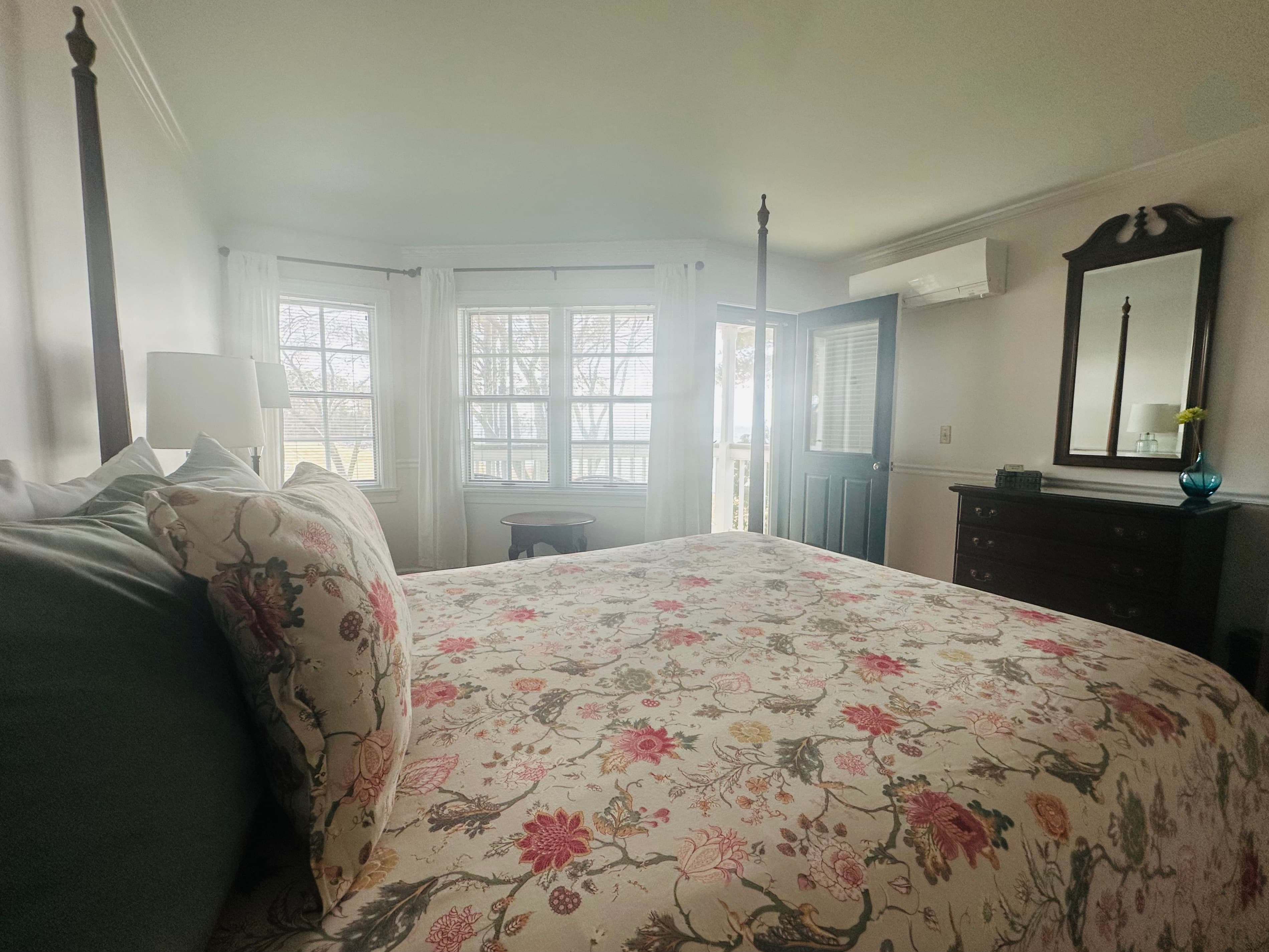 Cozy bedroom featuring a floral-patterned bedspread, large windows, and a rustic dresser.