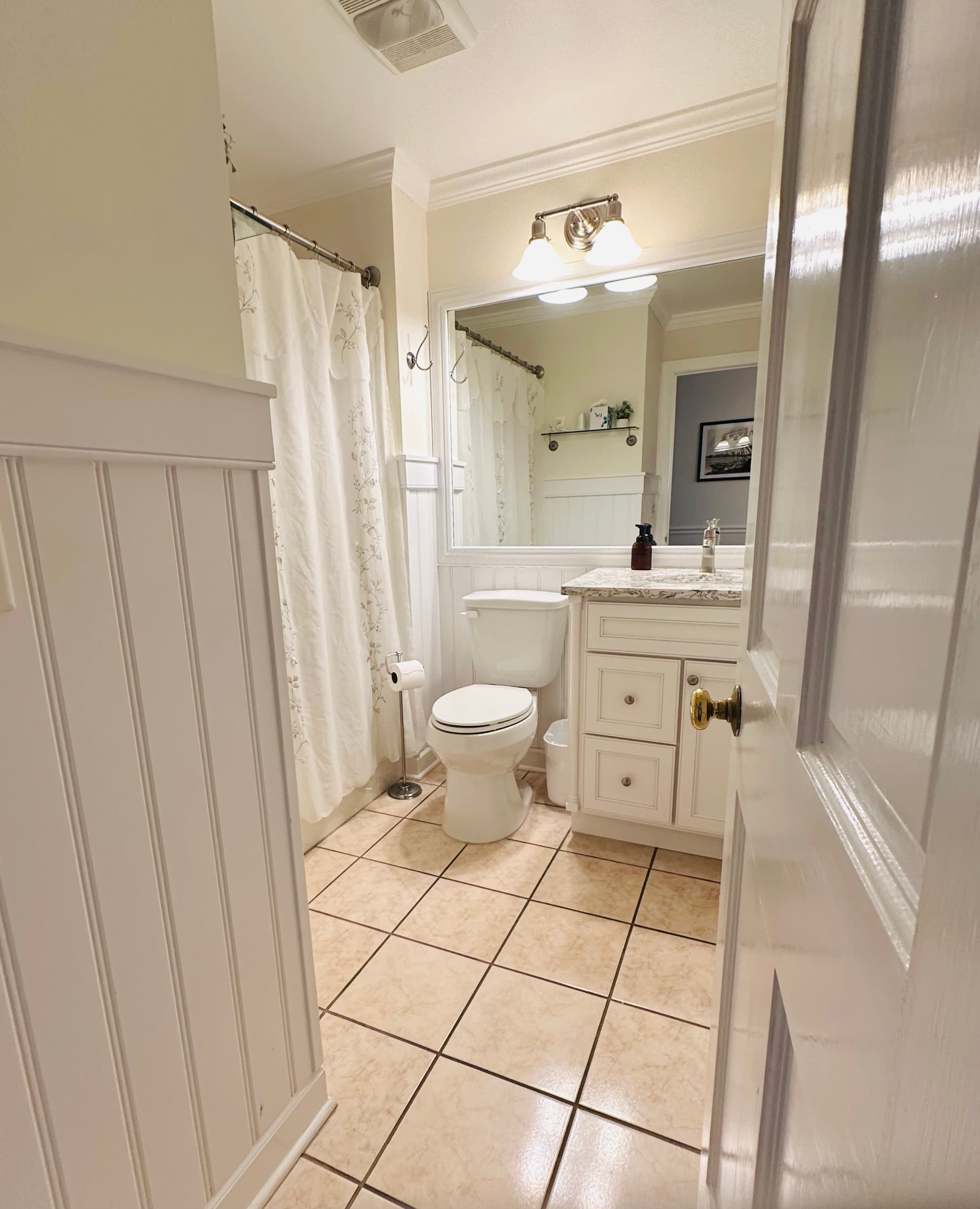 A well-lit bathroom featuring a toilet, sink with granite countertop, and a shower curtain.