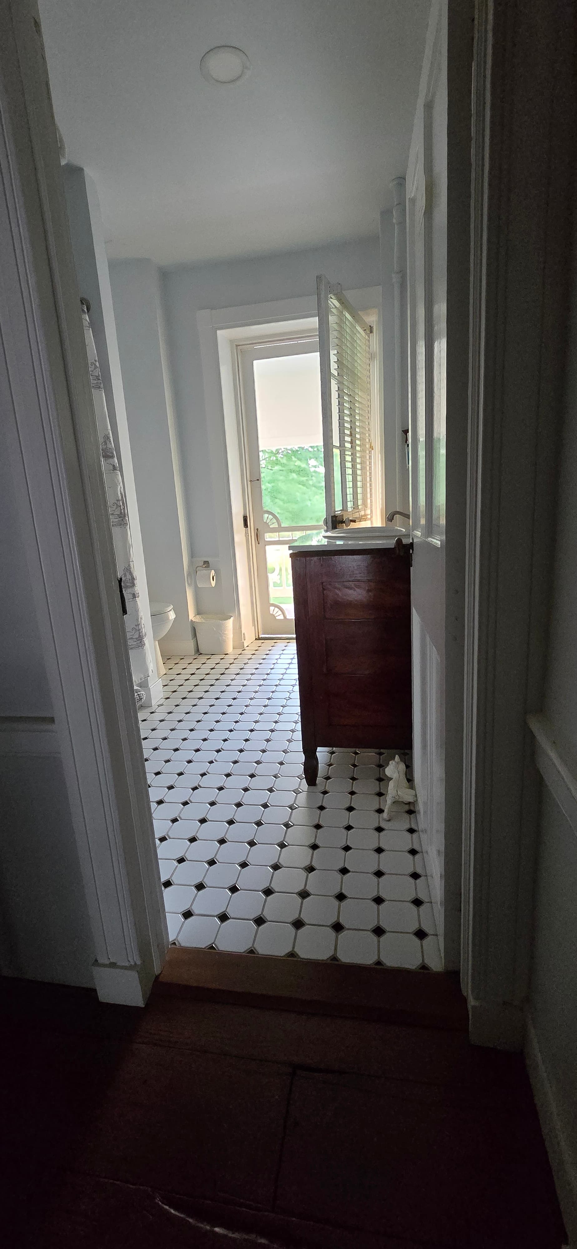 View down a hallway leading to a bathroom with tiled flooring and an open door to a patio.