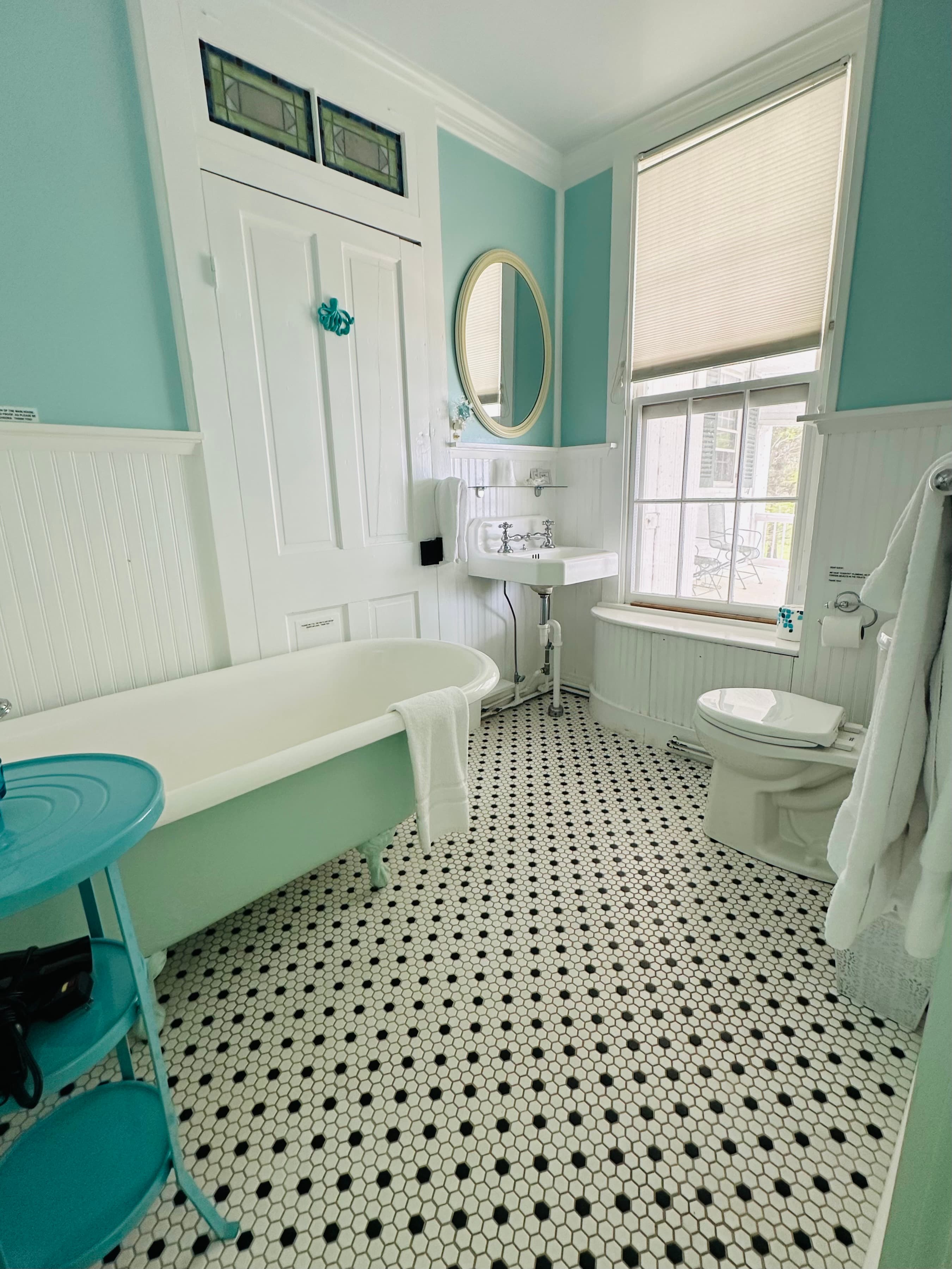 A bright, turquoise bathroom featuring a clawfoot tub, a pedestal sink, and patterned black and white flooring.