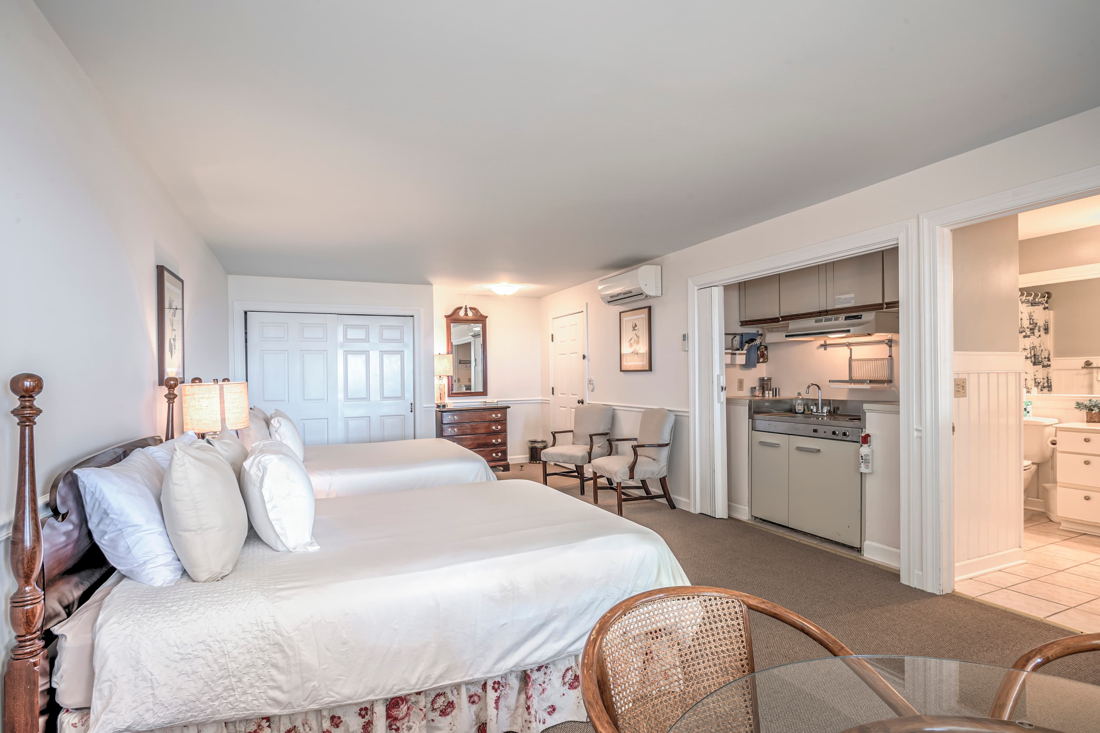 A spacious hotel room with two beds, a kitchenette, and a bathroom.