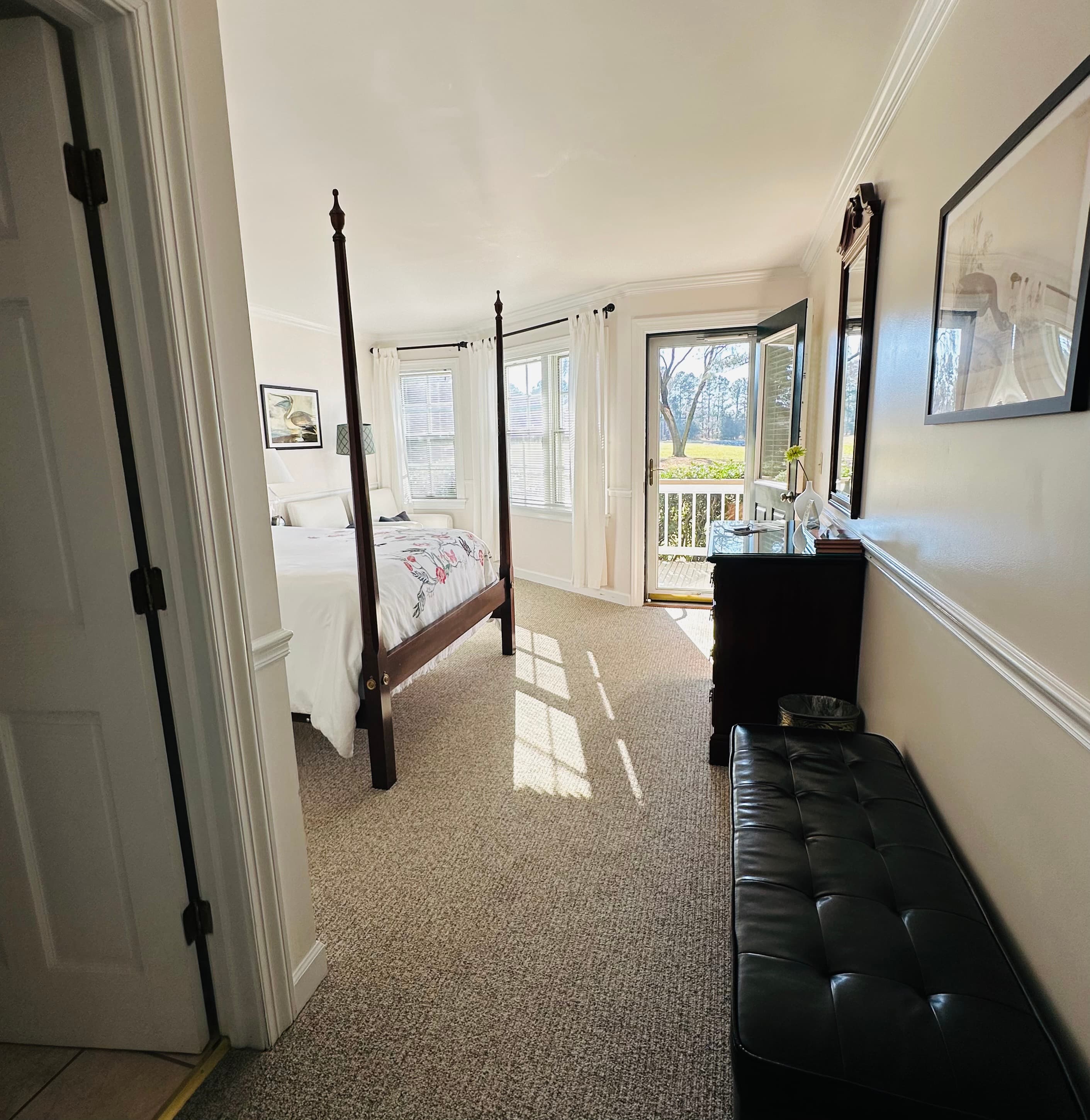 Bright and inviting bedroom with a four-poster bed, large windows, and an open door leading to a balcony.