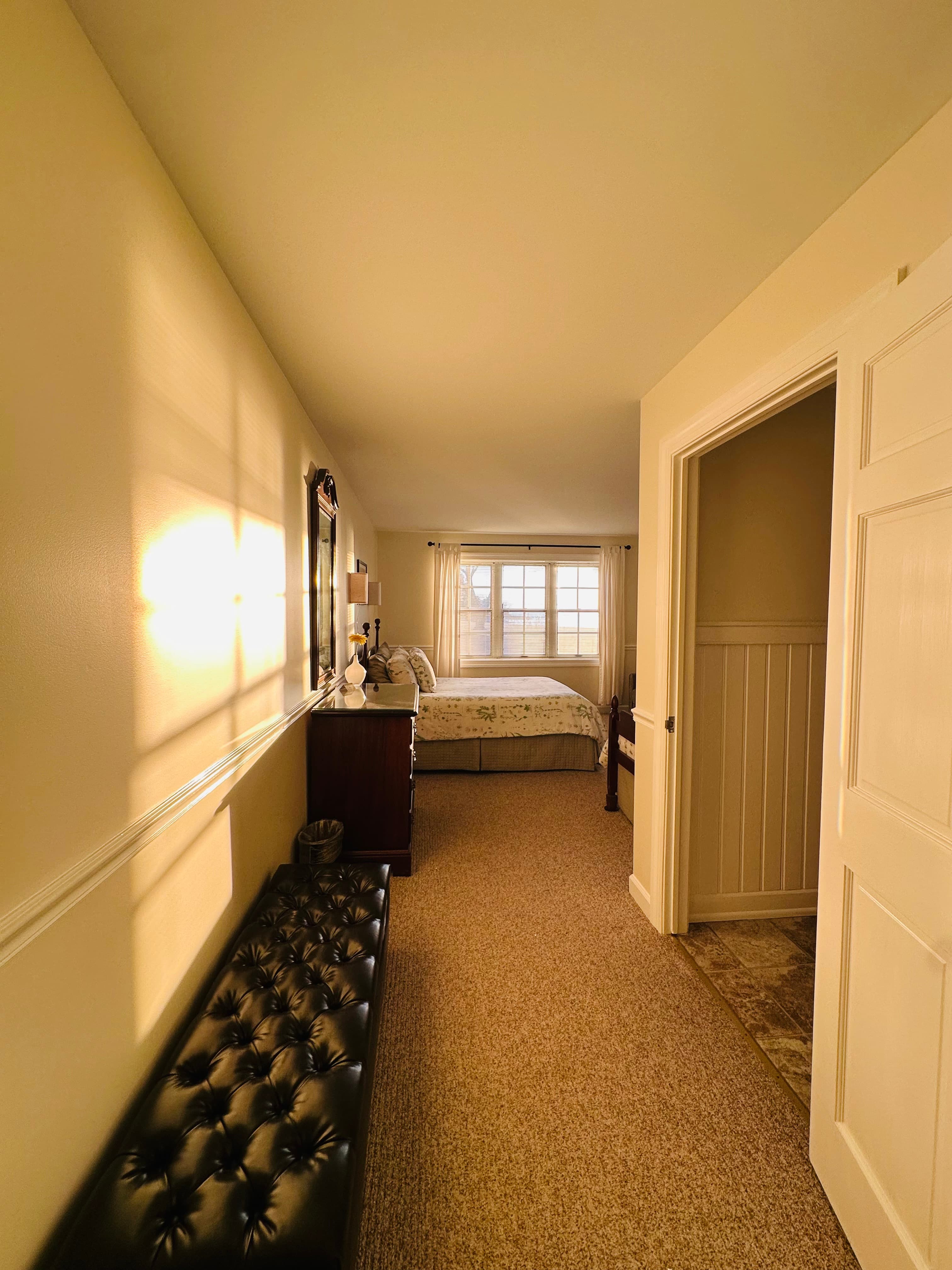 A softly lit hallway leads to a cozy bedroom with a window and floral bedding.
