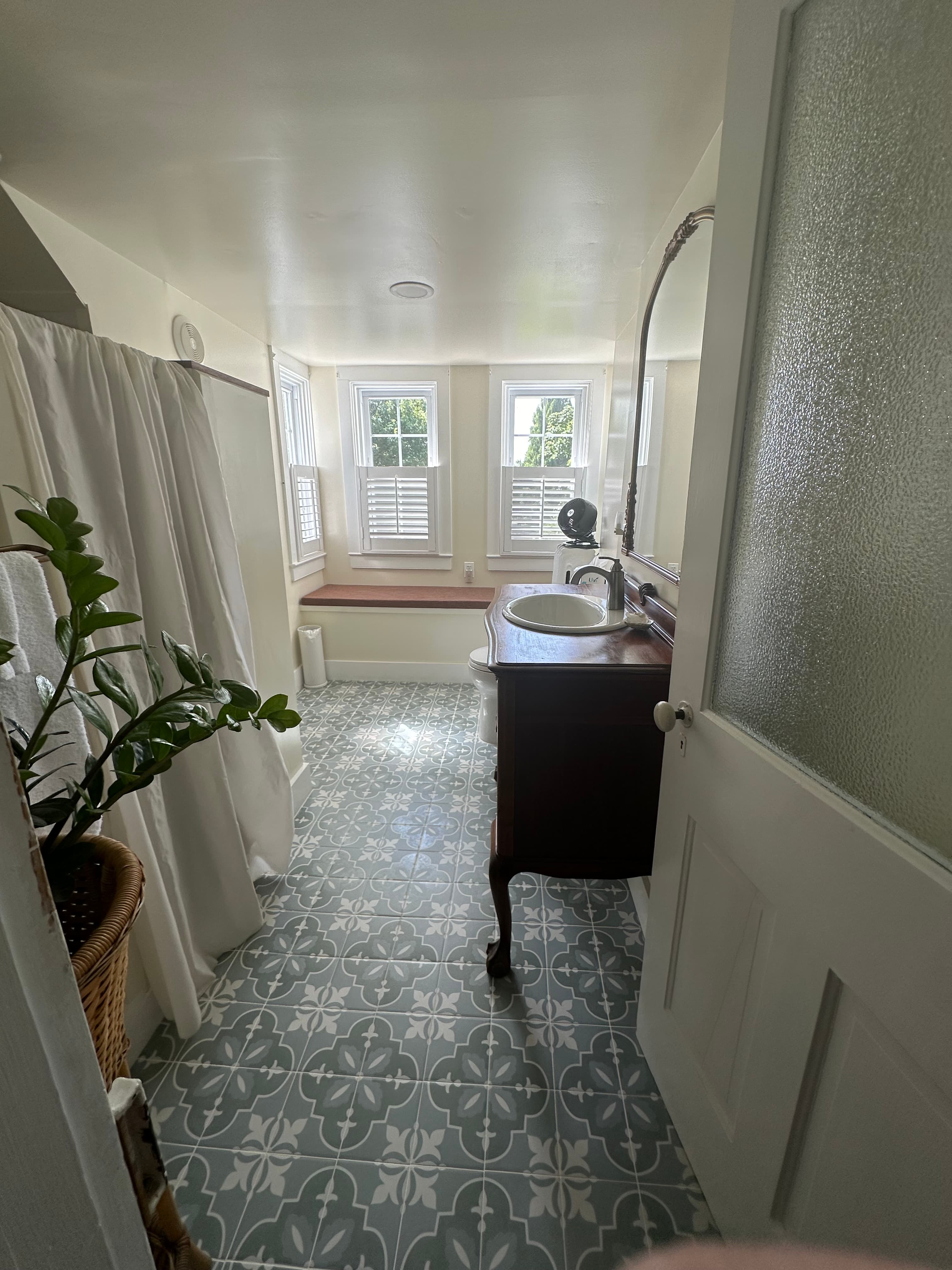 A bright, serene bathroom featuring a vintage sink, large windows, and patterned tiles.