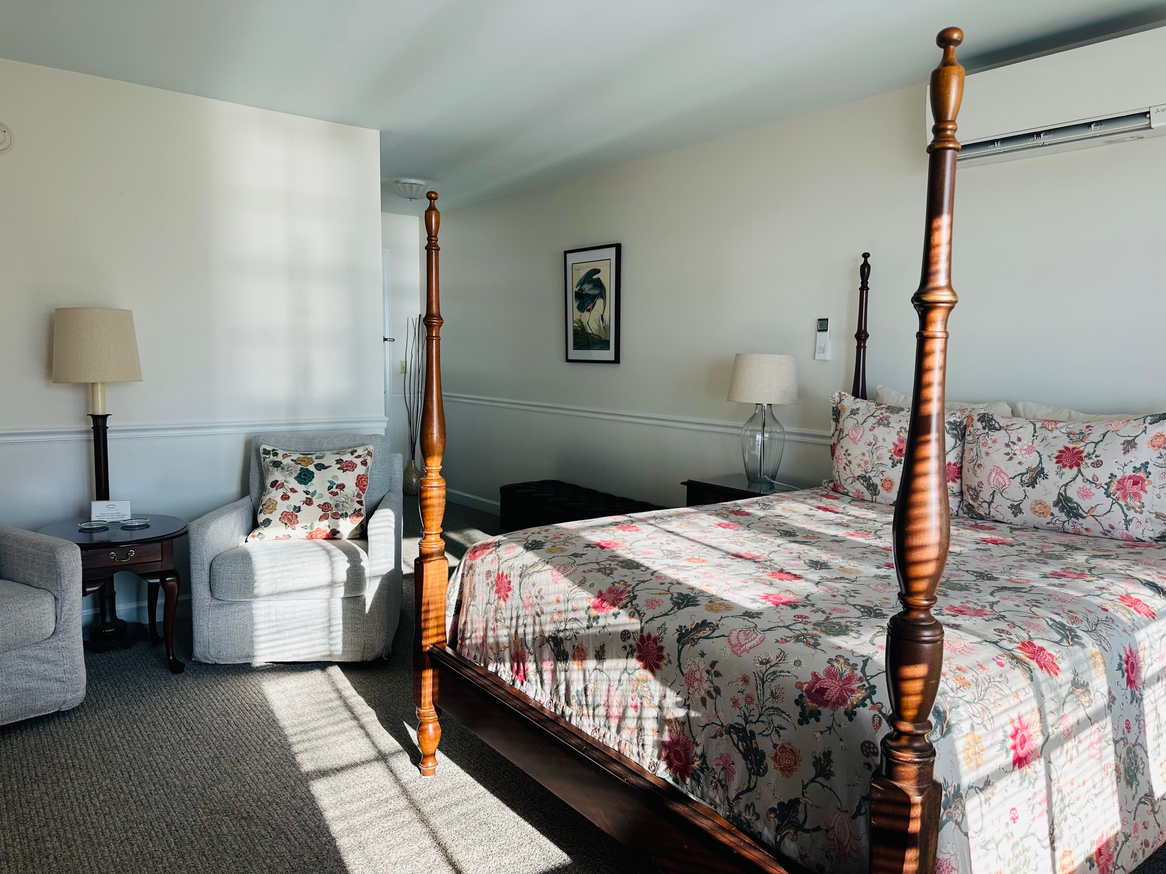 A bright and cozy bedroom featuring a four-poster bed, floral bedding, and a comfortable armchair.