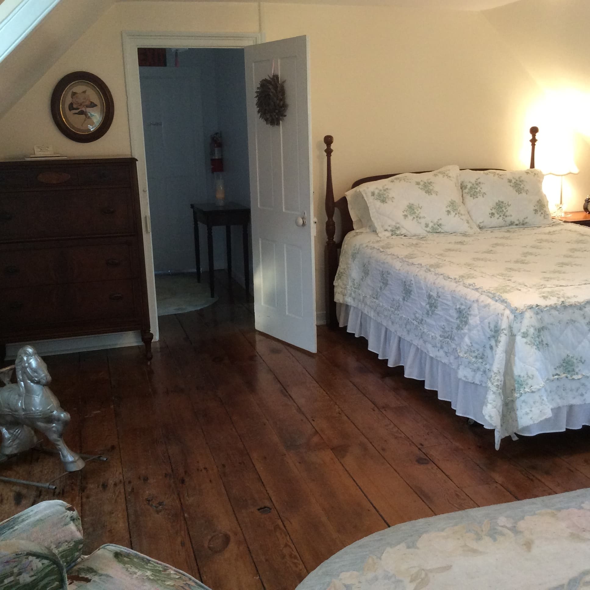 Cozy bedroom with a floral-patterned bedspread, wooden floors, and antique furniture.