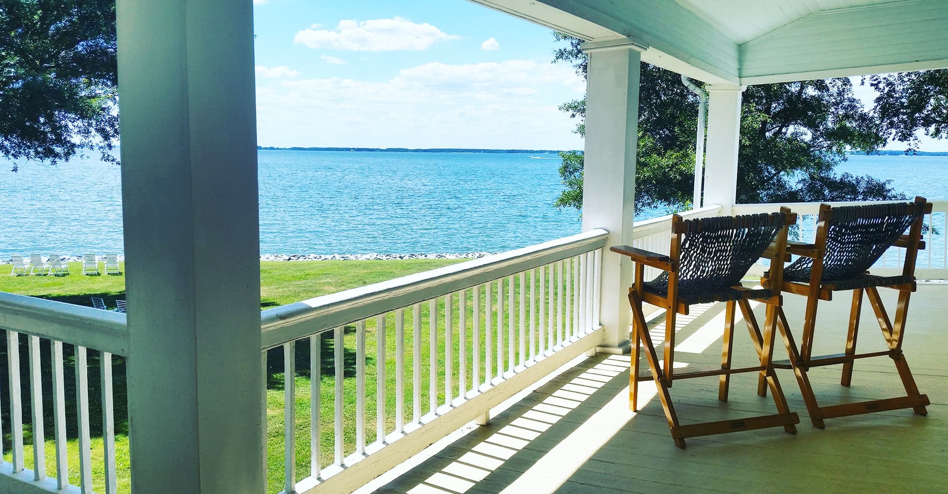 A serene lakeside view from a porch with two wooden chairs.