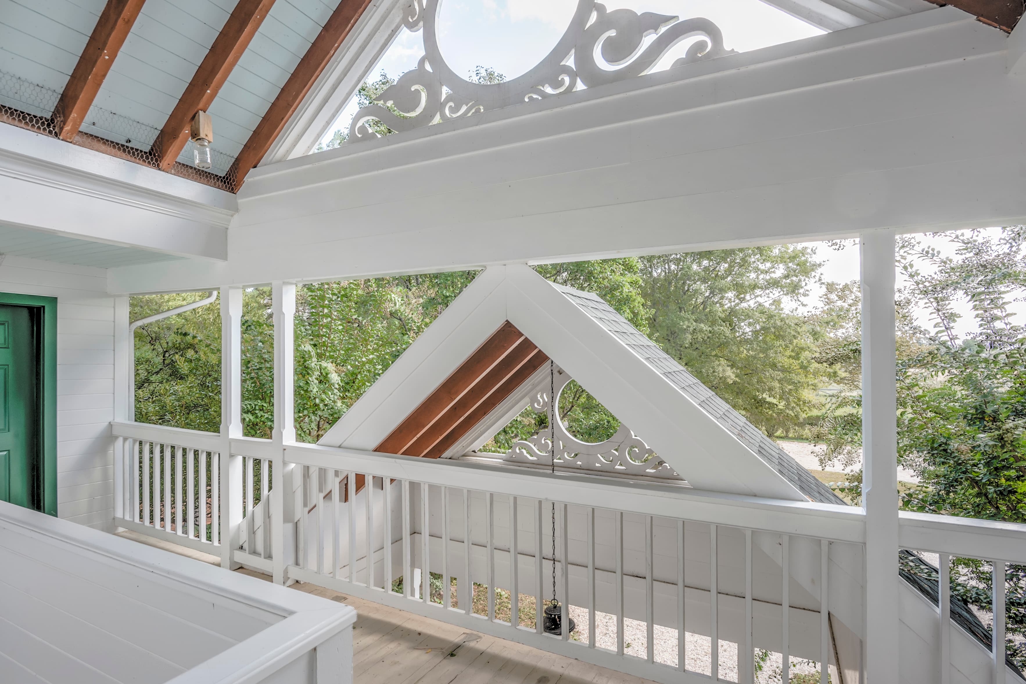 A bright, airy balcony with white railings and wooden beams overlooks lush greenery.