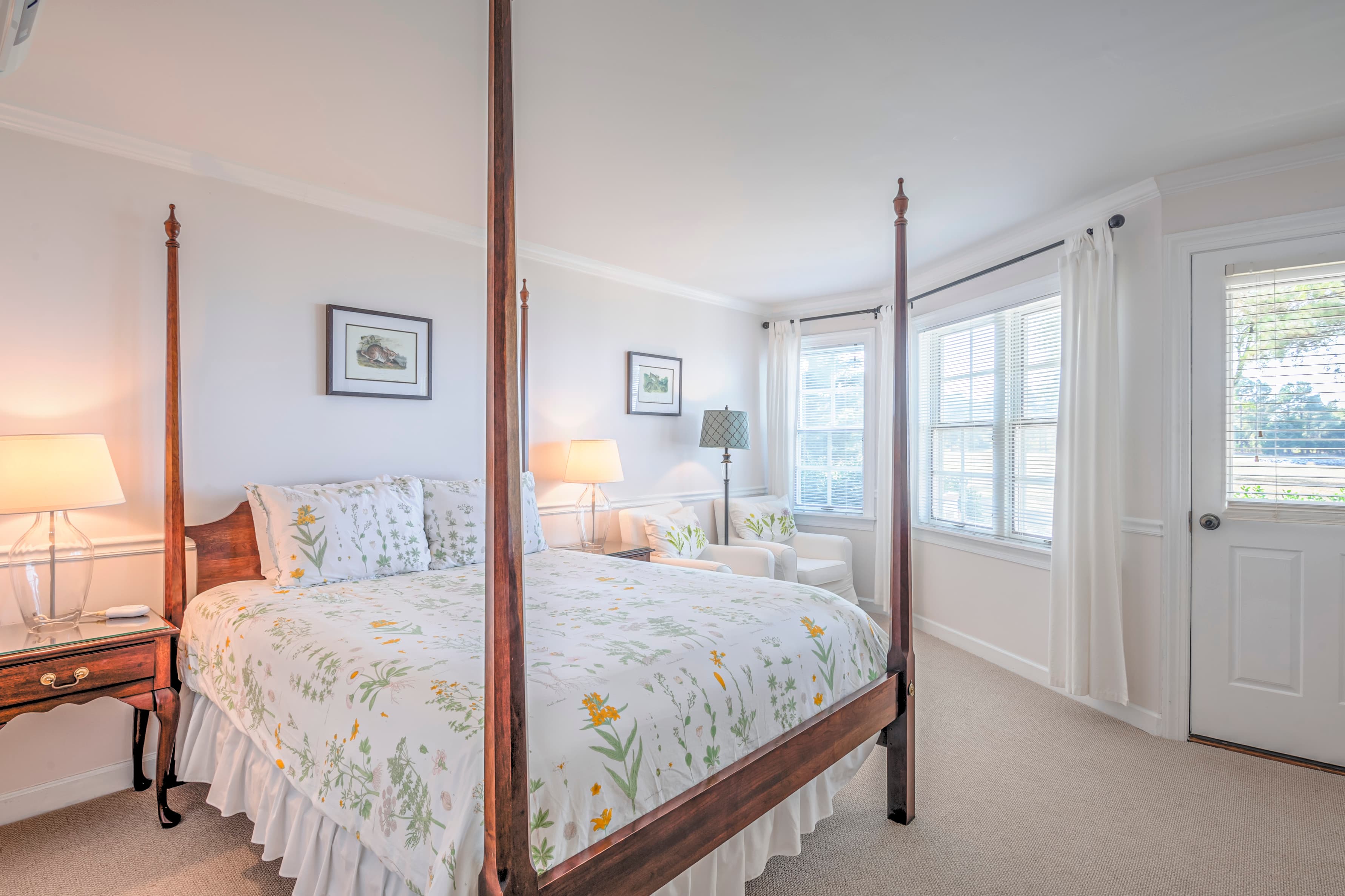 Bright, airy bedroom with a four-poster bed, floral bedding, and large windows.