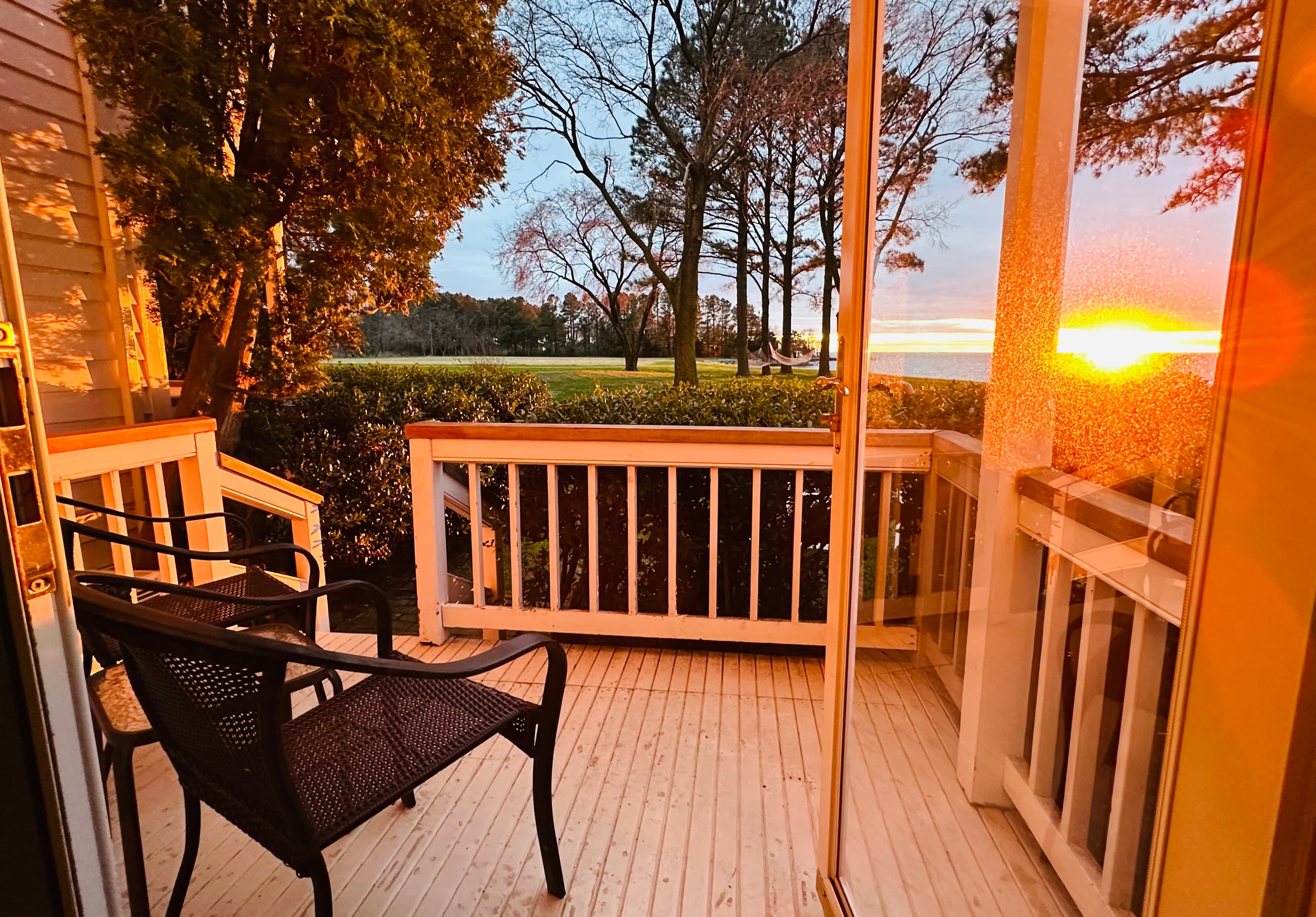 A cozy balcony with two black chairs overlooking a sunset view.