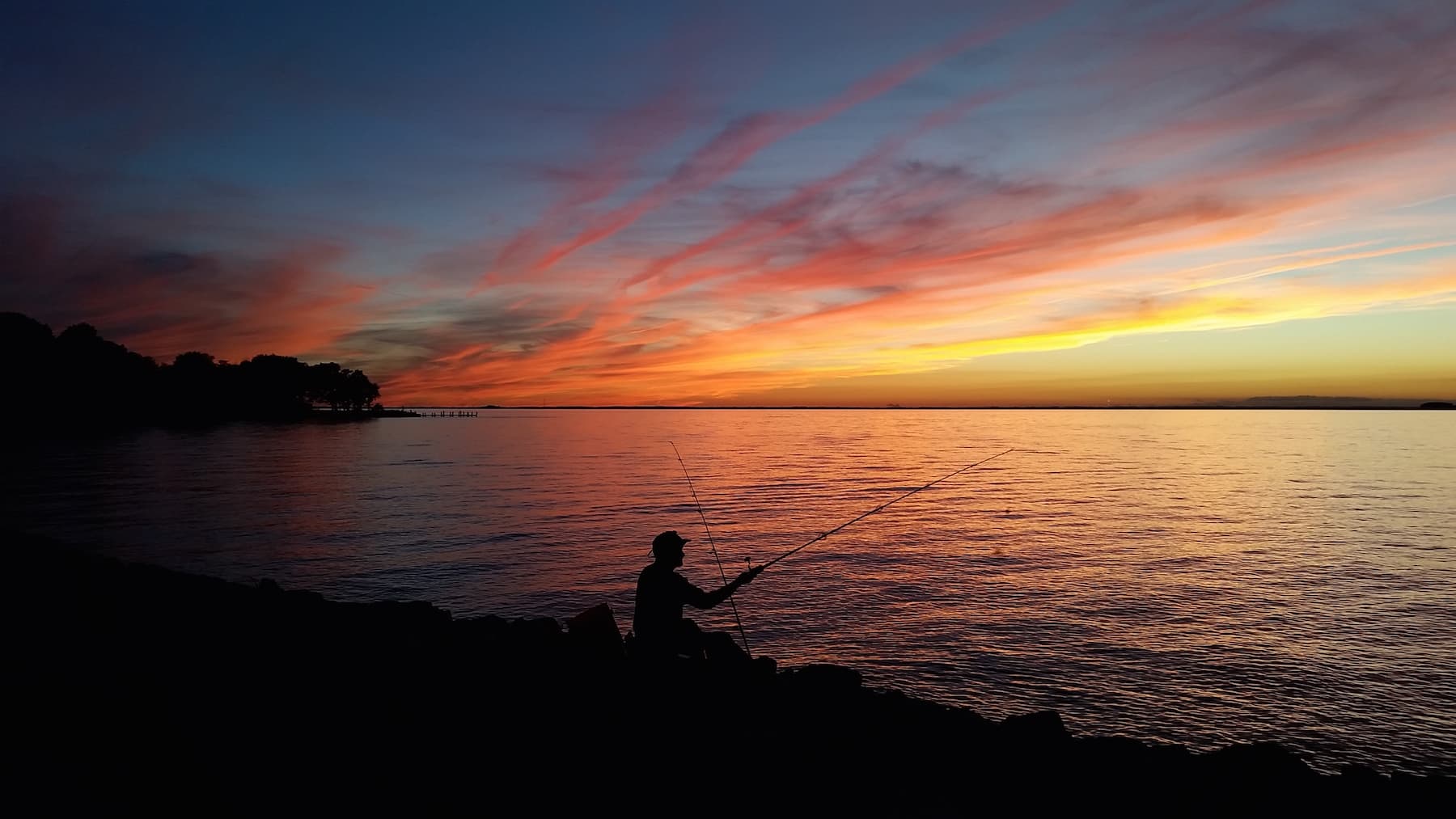 A silhouette of a person fishing at sunset over a calm lake. A silhouette of a person fishing at sunset over a calm lake.