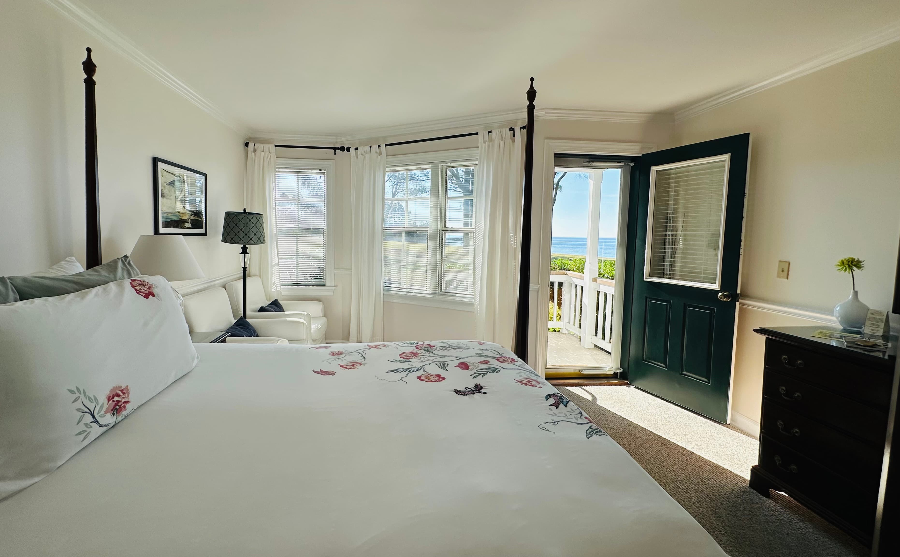 A bright bedroom with a large bed, open door to a patio, and windows offering views of the nearby beach.