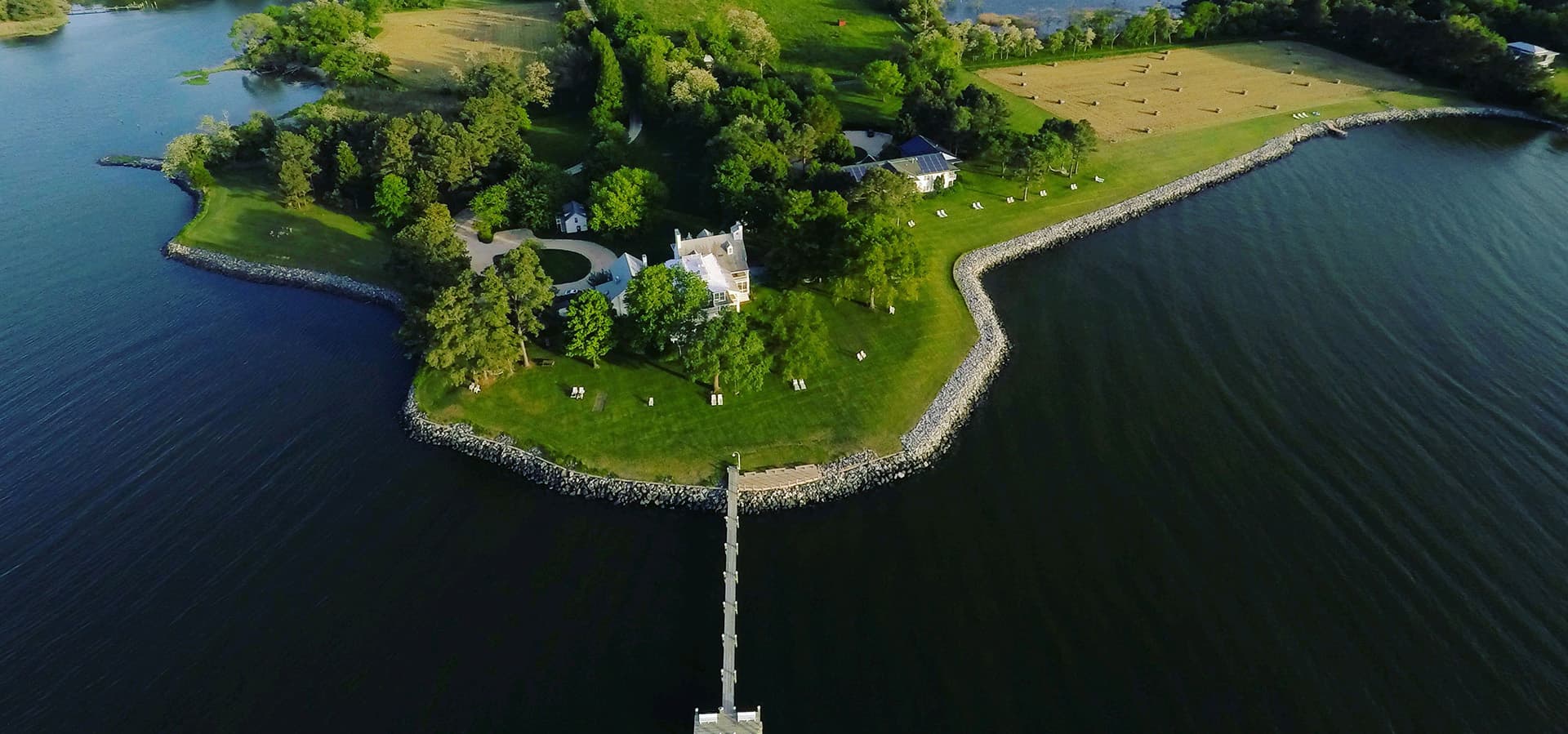 Aerial view of a small, lush island with a house surrounded by water and a jetty.