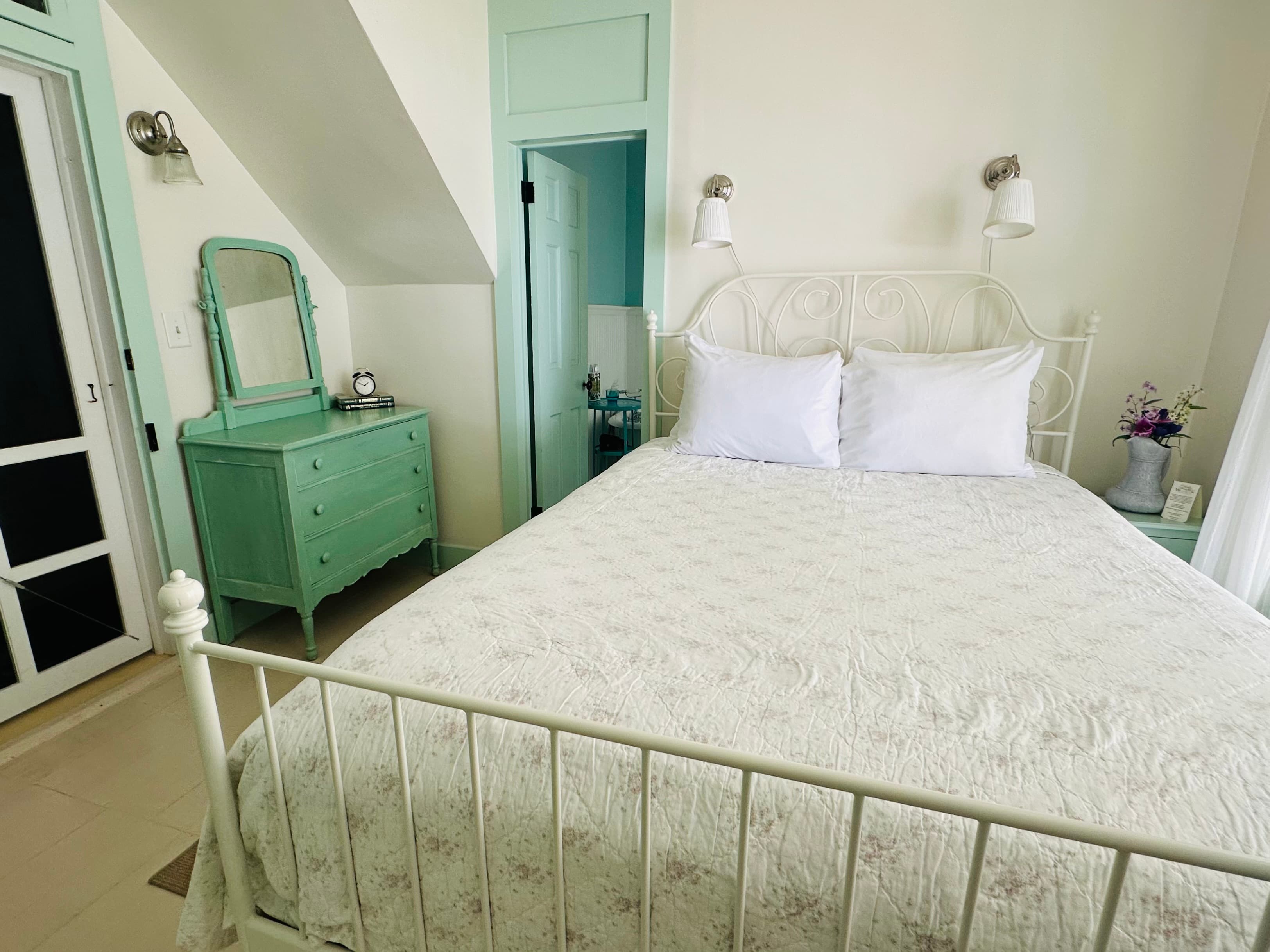 A cozy bedroom featuring a white iron bed, light bedding, and mint green accents with a dresser and mirror.