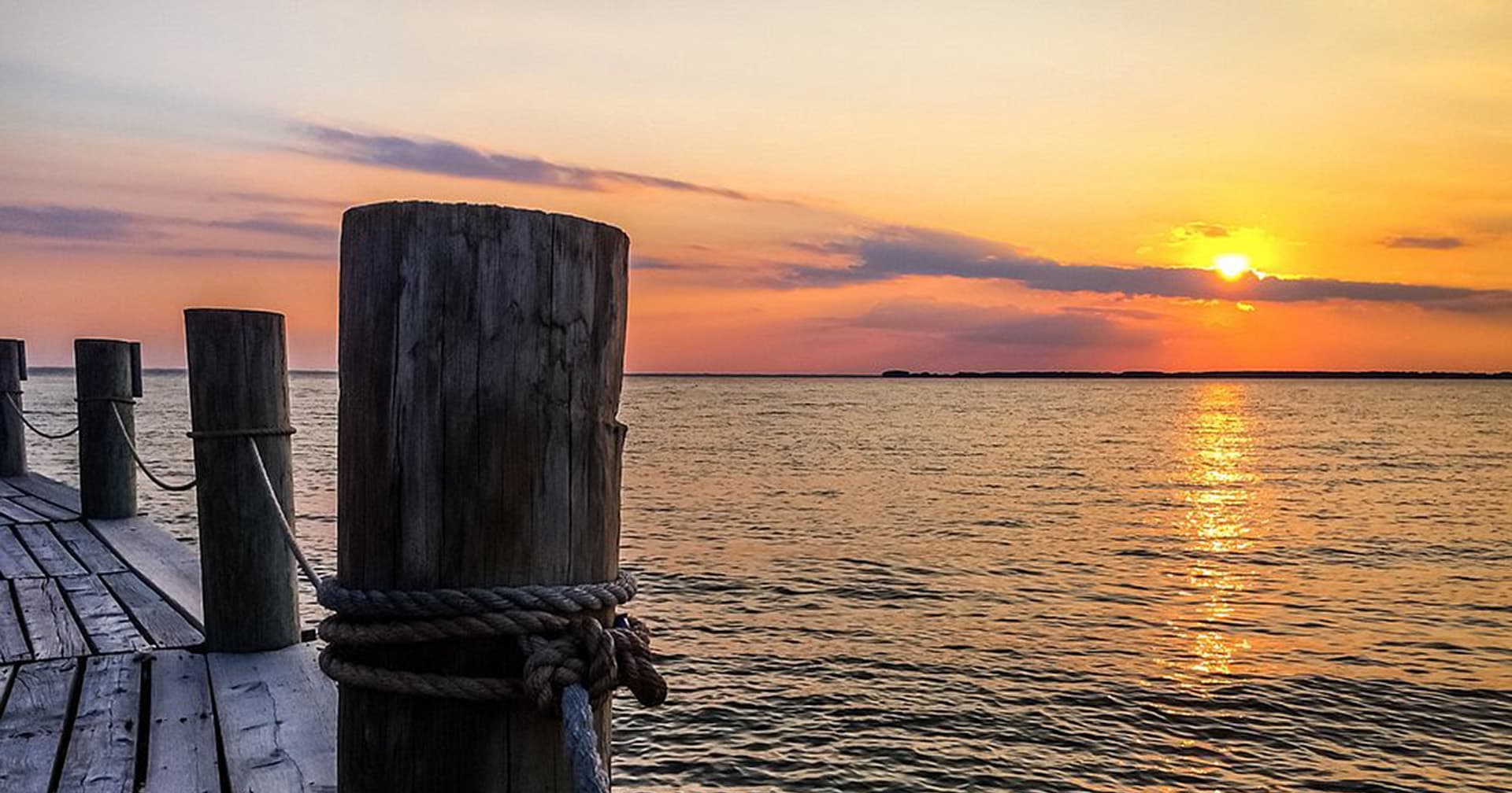 A wooden dock with a weathered post, overlooking a tranquil sunset over the water.