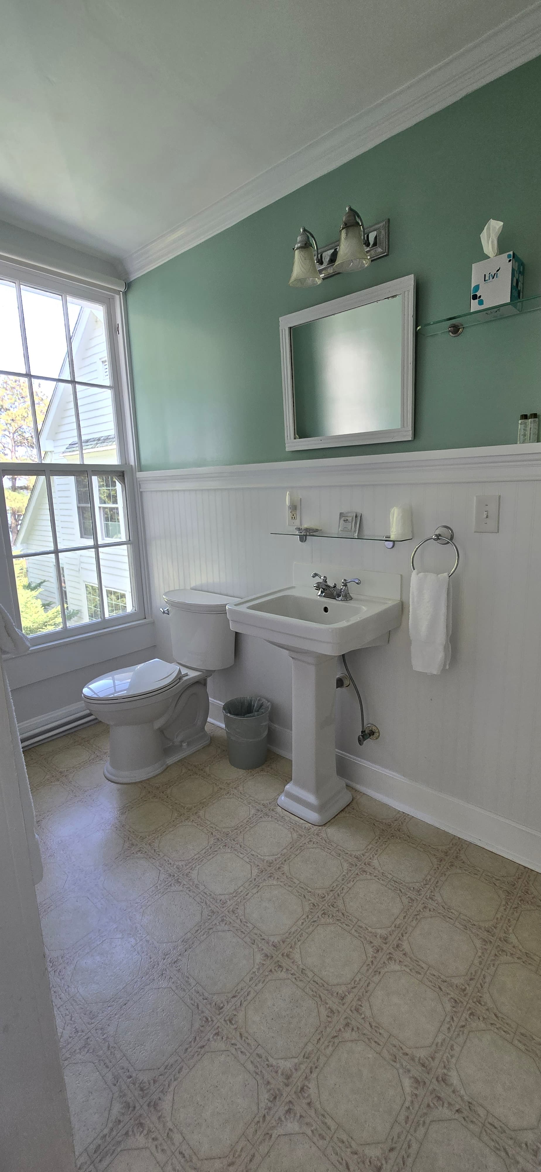 A bright bathroom featuring a sink, toilet, and large window with green walls.