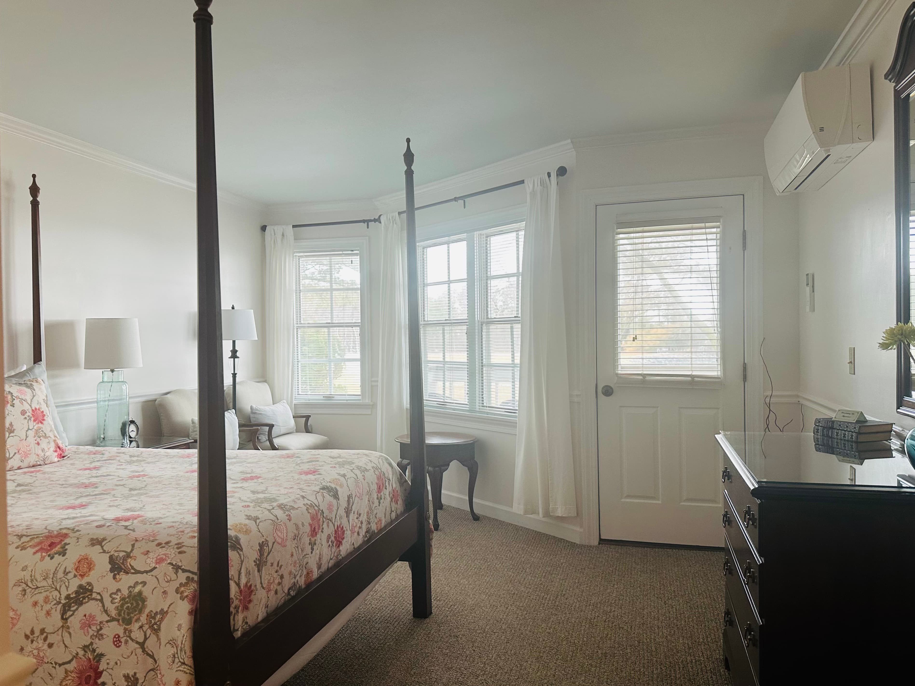 Bright bedroom featuring a four-poster bed, large windows with sheer curtains, and a bedside table.
